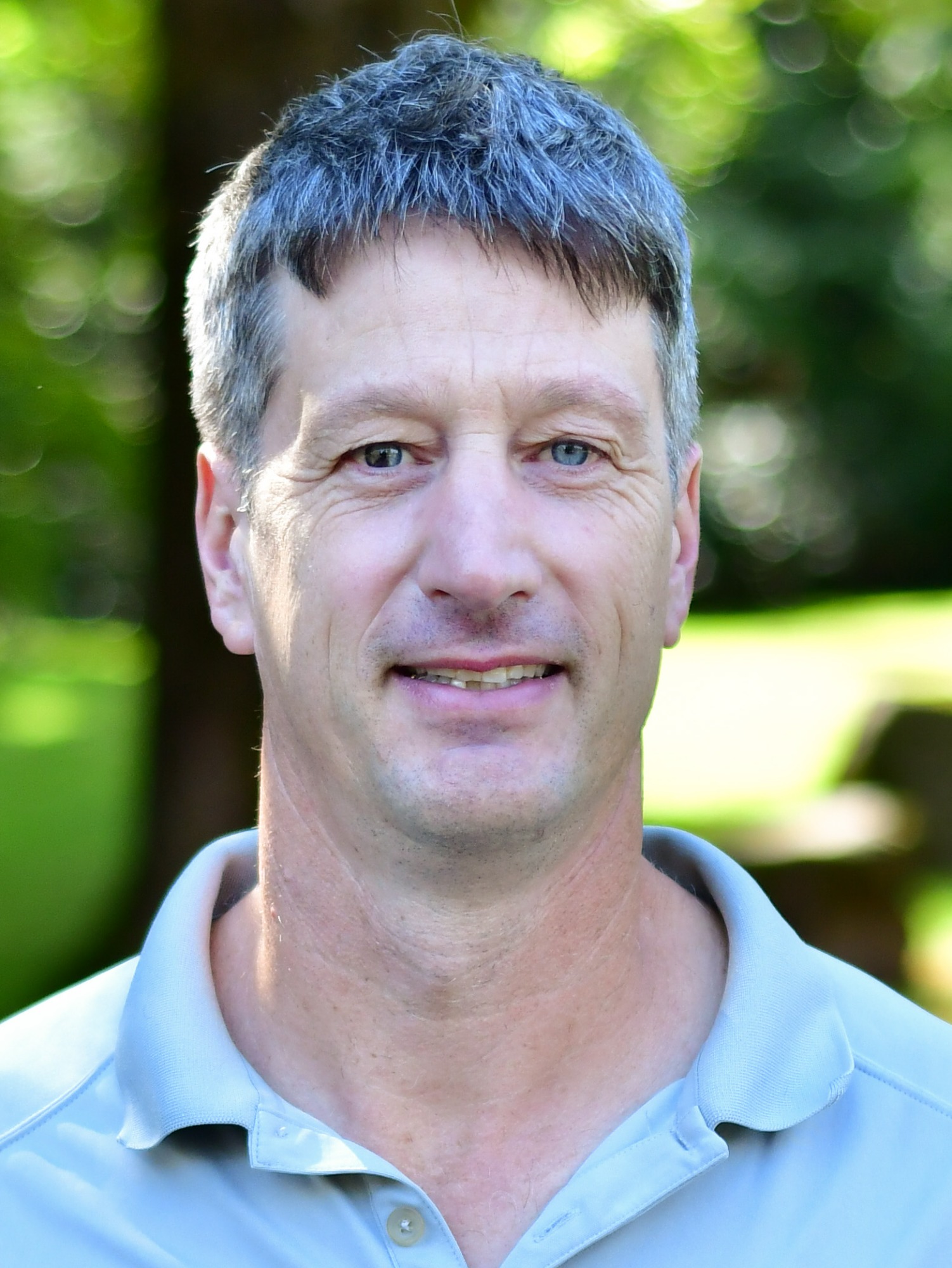 Brad Johnson stands outside in front of a green background, smiling.