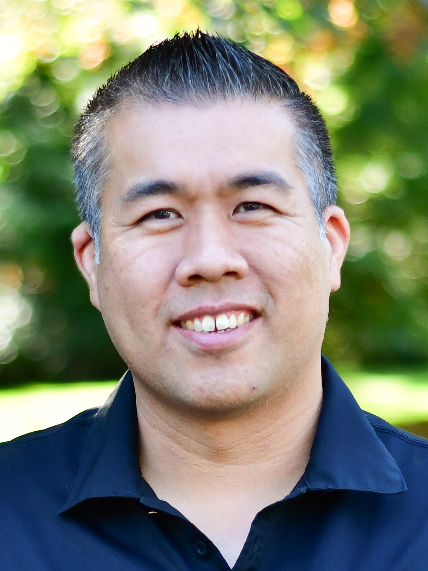 Jimmy Chau stands outside in front of a green background, smiling.