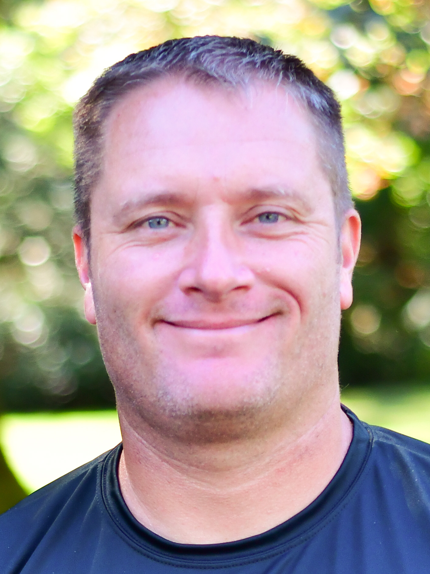 Matt Kosderka stands outside in front of a green background, smiling.