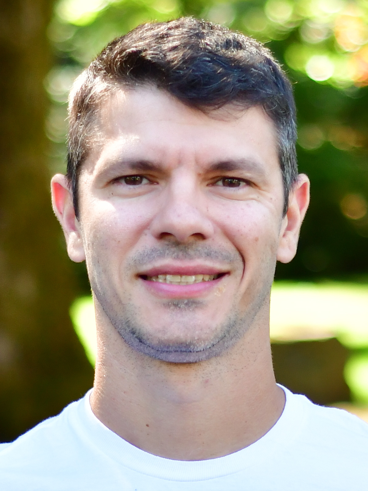 Murilo Martins stands outside in front of a green background, smiling.