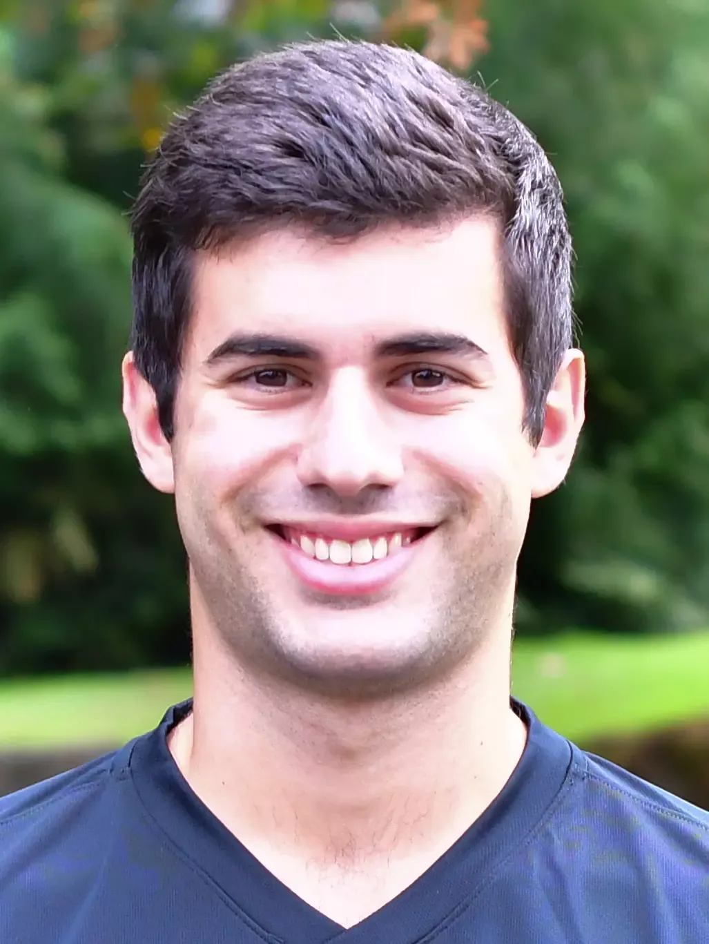 Kristian Peev stands outside in front of a green background, smiling.