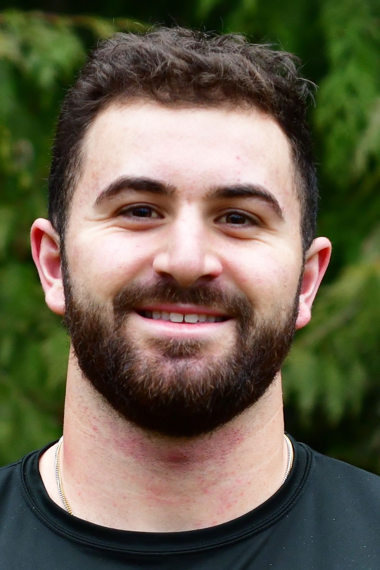 Jack Thomson stands outside in front of a green background, smiling.