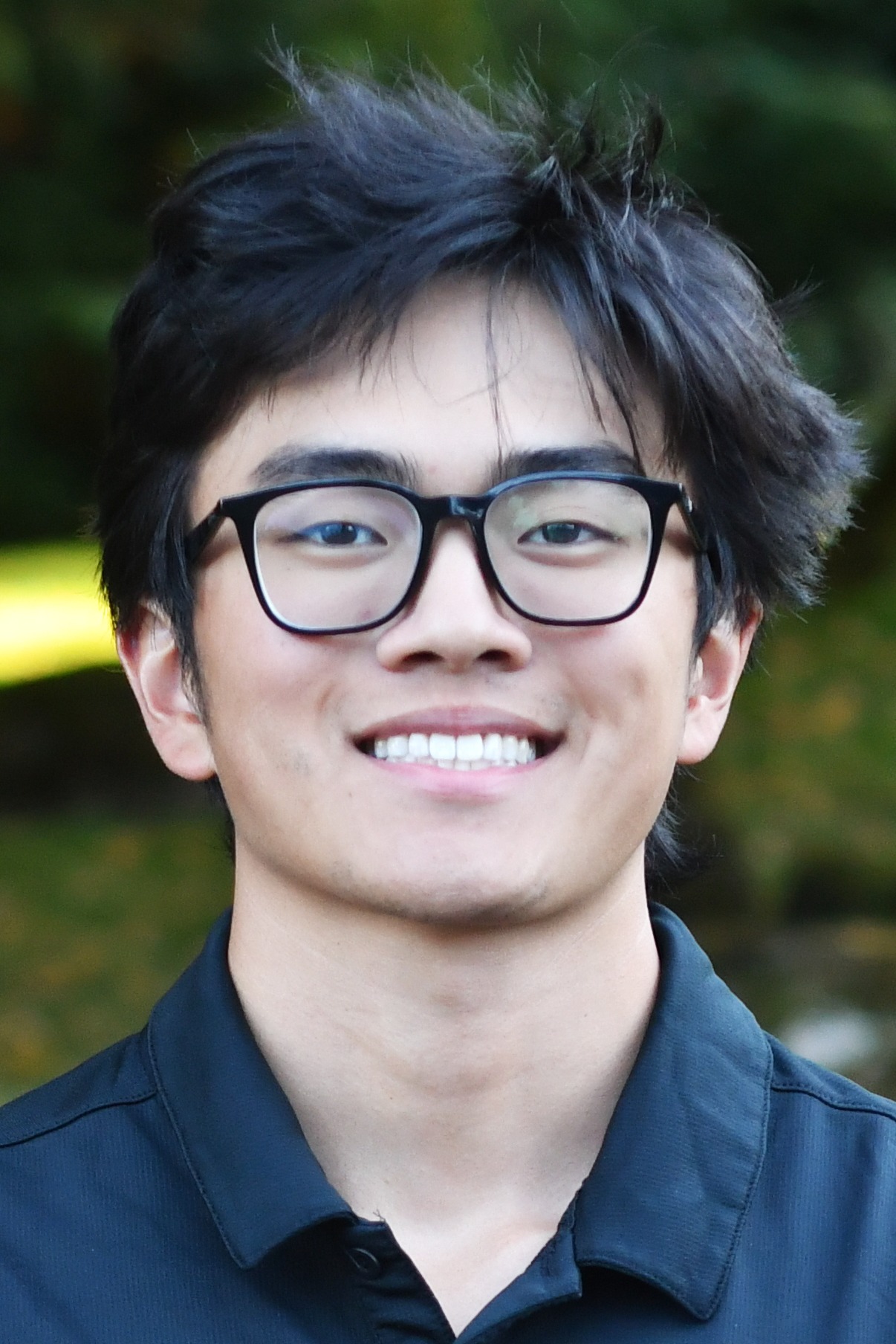 Johnny Pang stands outside in front of a green background, smiling.