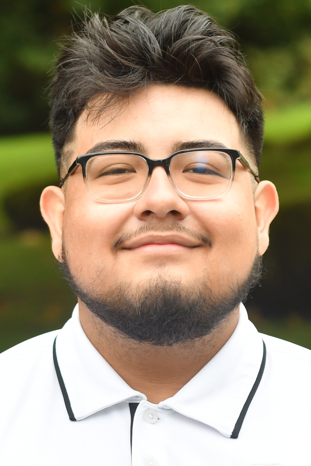 Eliel Martinez stands in front of a green background smiling.