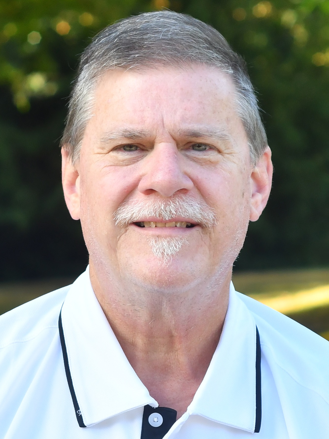 Bruce Read stands outside in front of a green background, smiling.