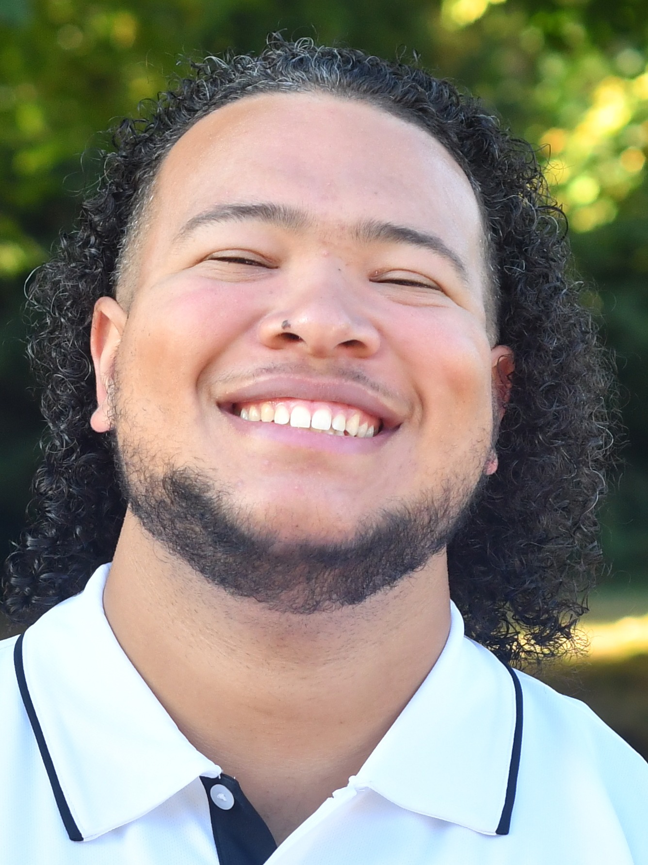 Eryk Schaftlein stands outside in front of a green background, smiling.