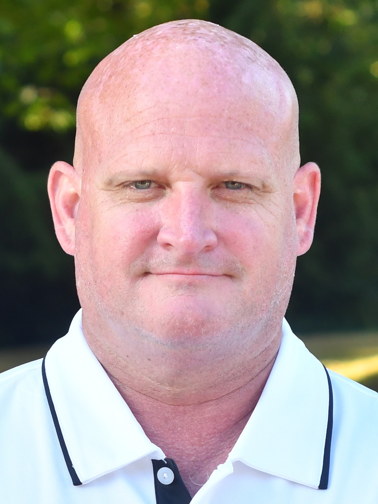 Randy Heath stands outside in front of a green background, smiling.