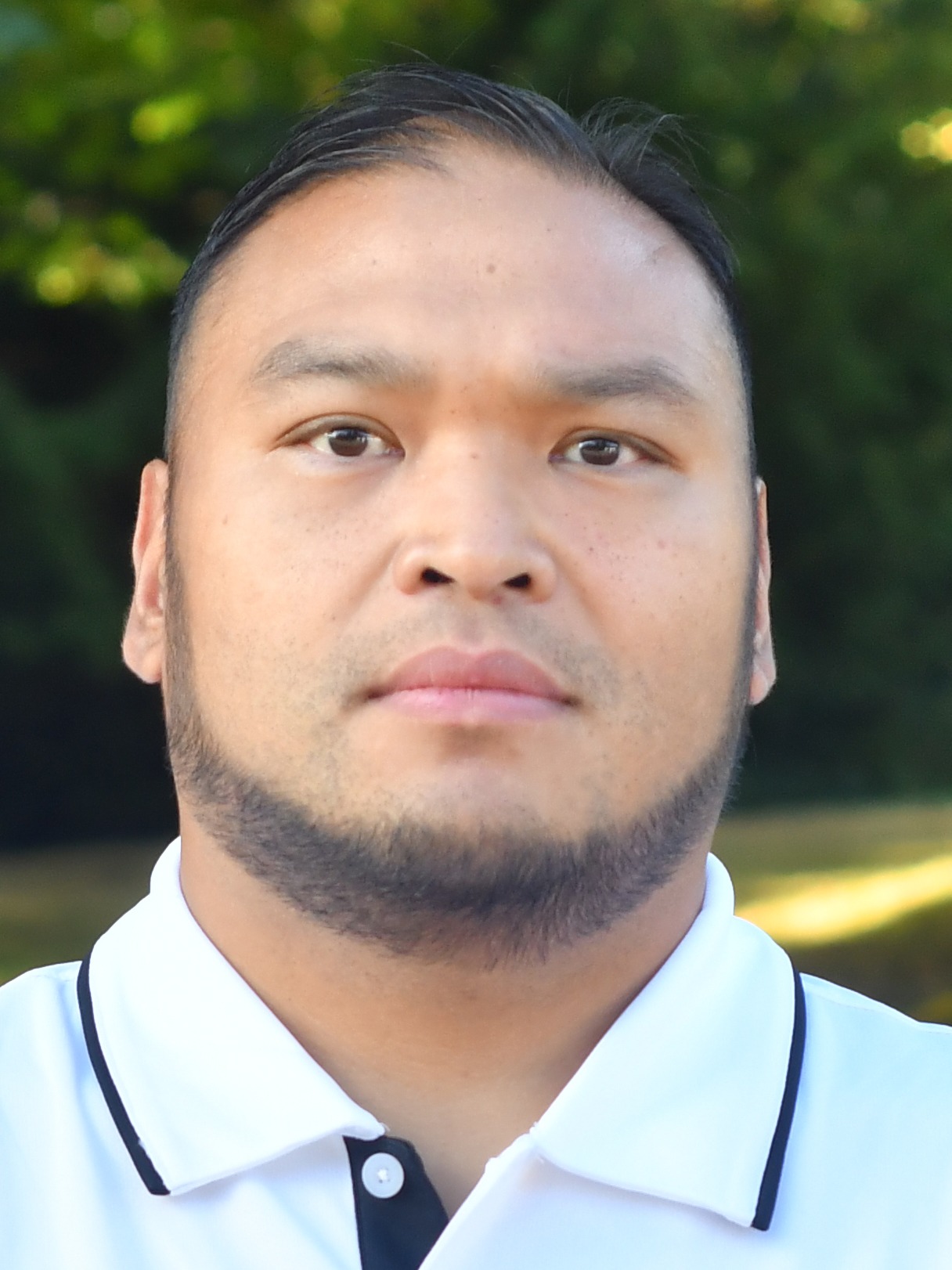Renato Felina stands outside in front of a green background, looking serious.