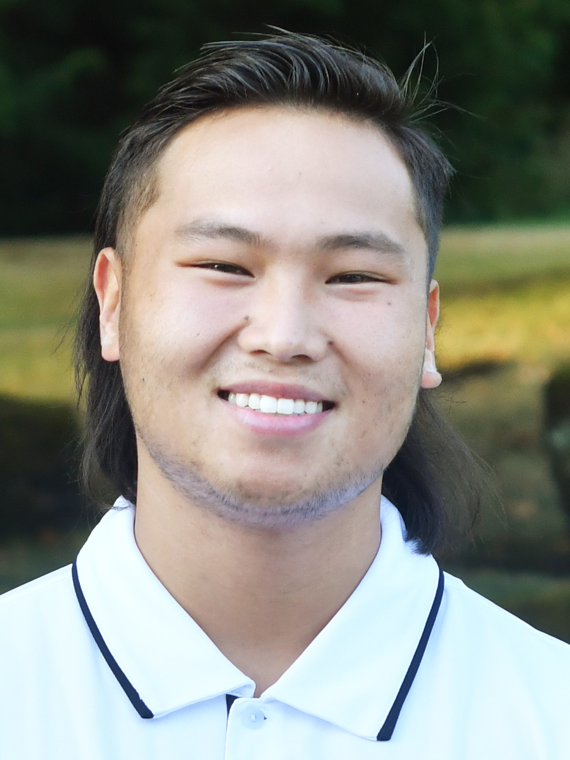 Rusty Nozoe stands outside in front of a green background, smiling.