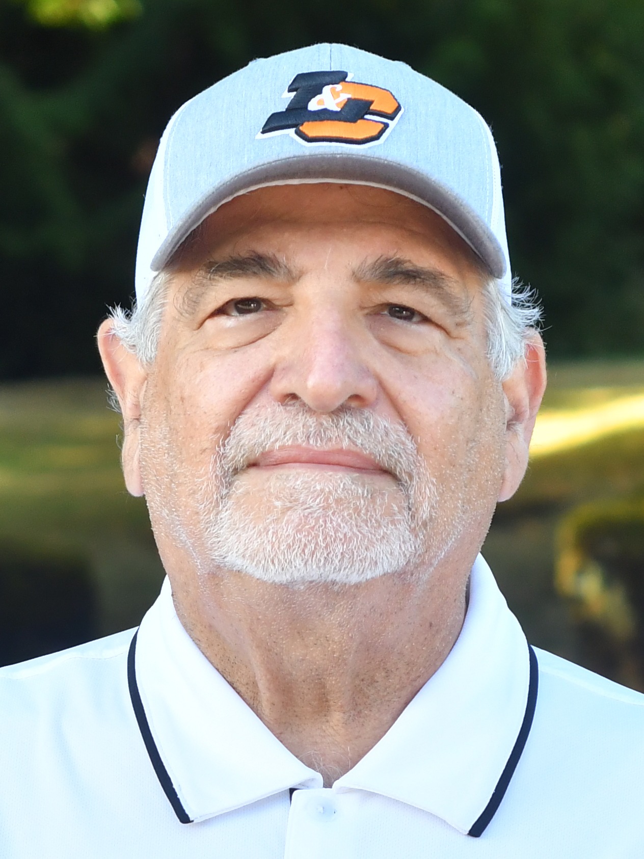 Tom Sunseri stands outside in front of a green background, looking serious.