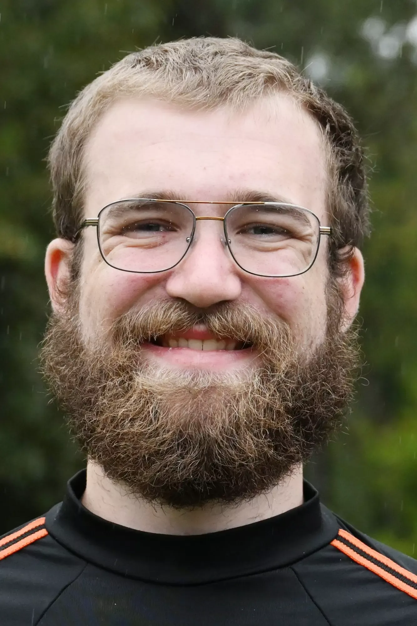Caleb Novotny stands in front of a green background, smiling.