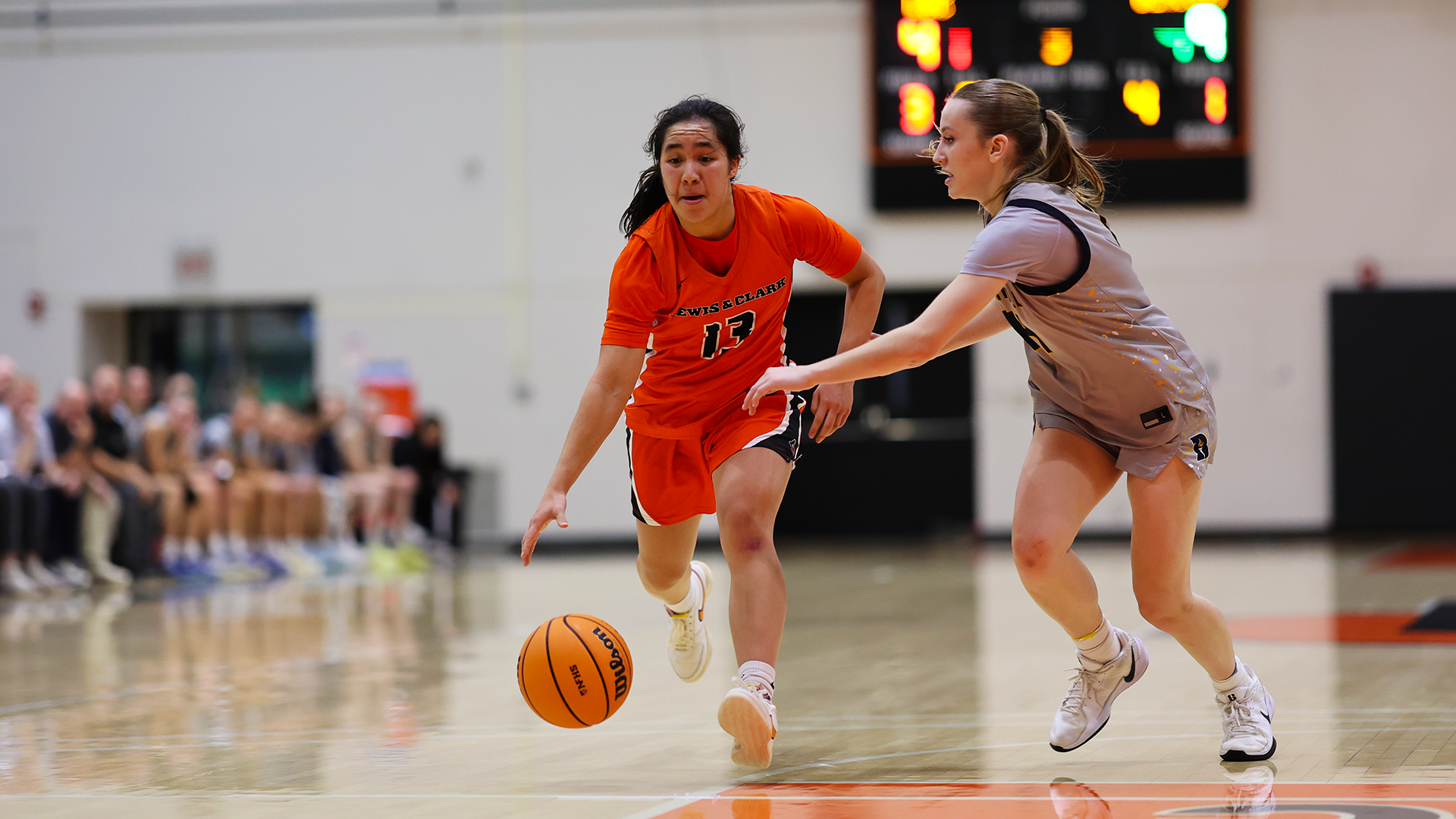Lilly Jordan in orange dribbles against a defender in gray to the basket. 