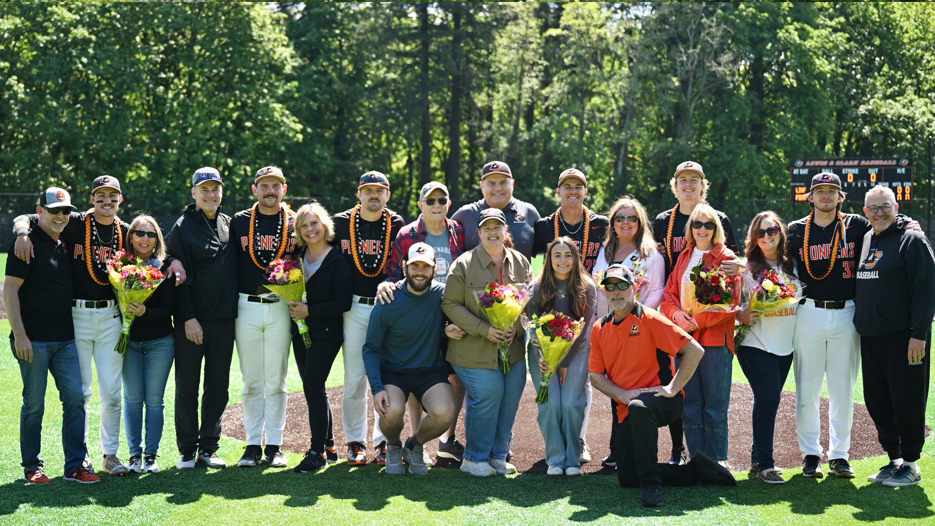 From left to right seniors Justin Cavagnaro, Luke Ritter, Will Heron, Brennen Davis, Ryan Harvey and Kyle Wilsie pose with their families on the baseball field with the trees and scoreboard in the background. 