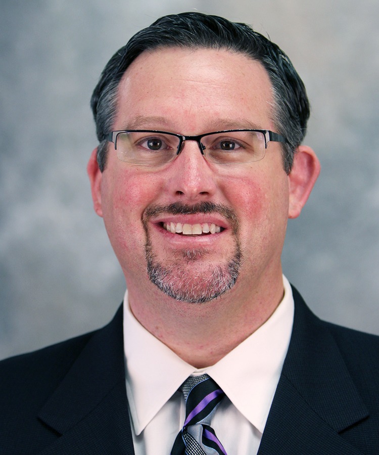 Shanan Rosenberg smiles in front of a gray backdrop.