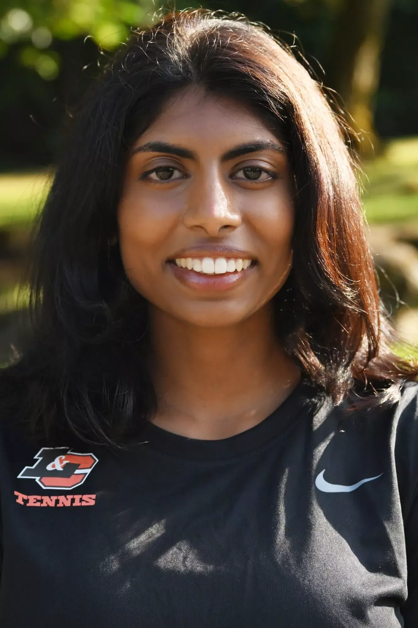 Susanna Anand stands in front of a green background smiling. 