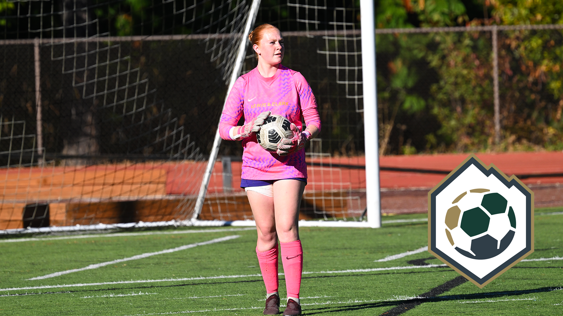 Mallory Symons stands in front of the goal holding the soccer ball.