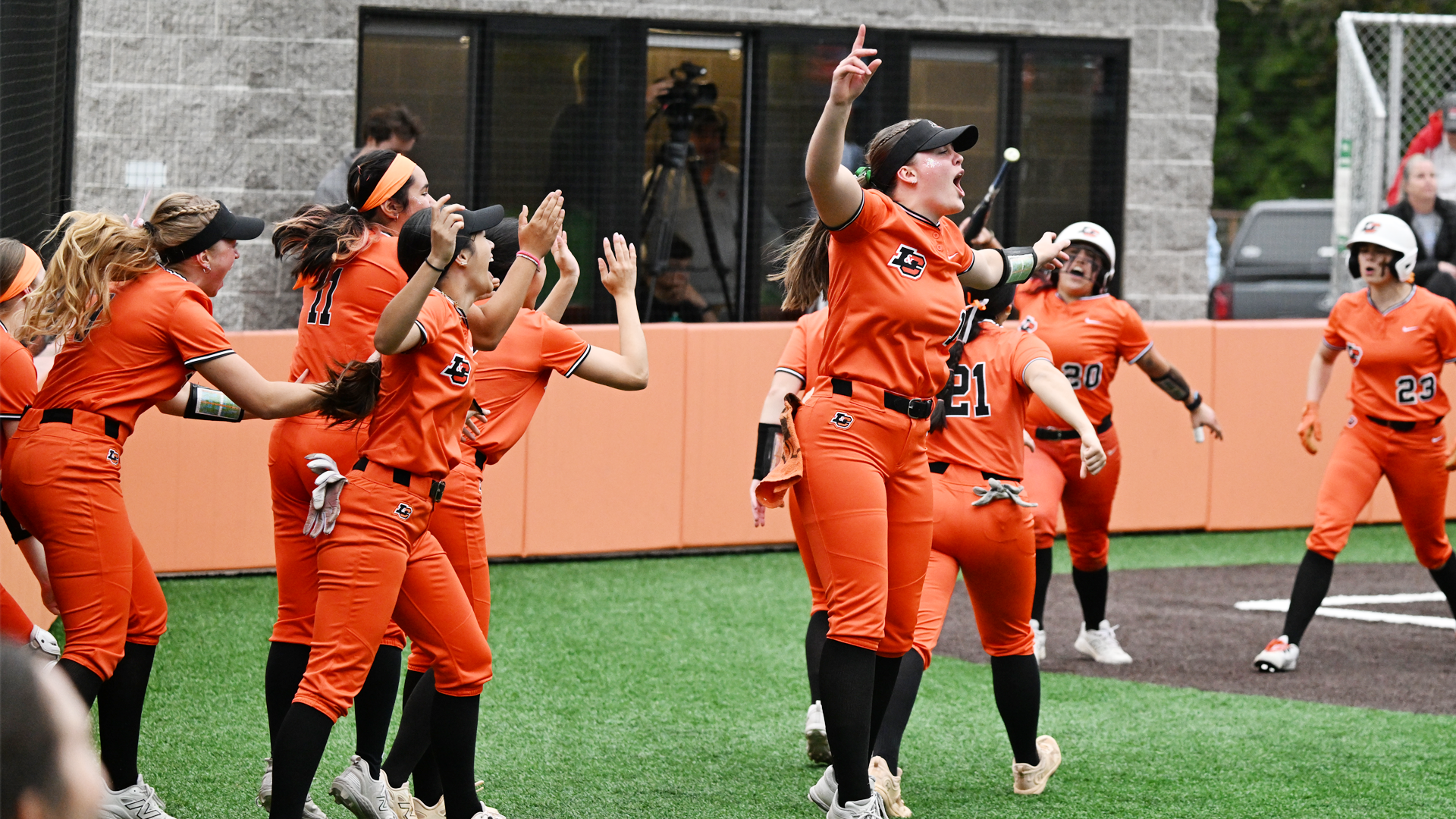 Softball players stream out of the dugout and jump up and down after defeating the Bennies