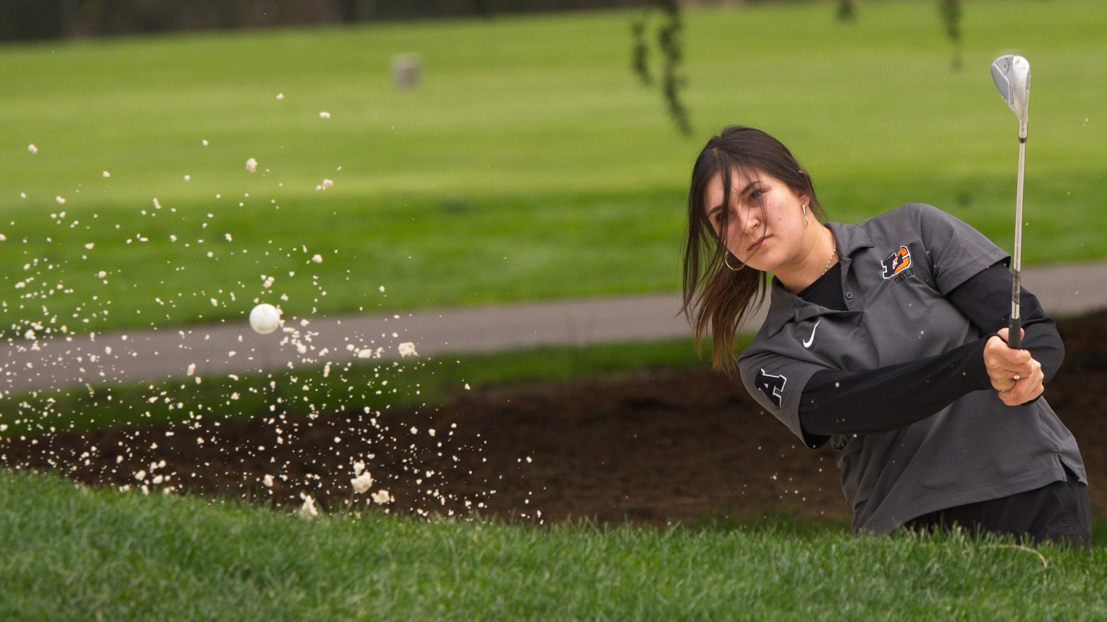 Julia Klenk hits a shot of the bunker and the sand and ball fly upward
