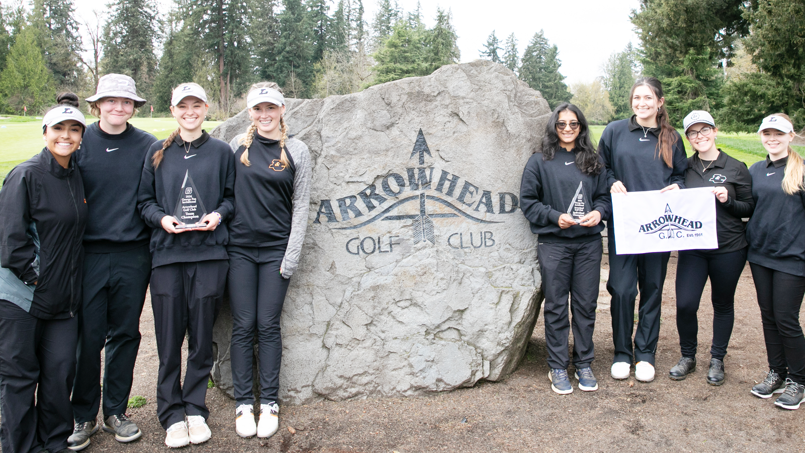 Women's Golf poses with the GFU Invitational Trophy in front of a giant rock that says 