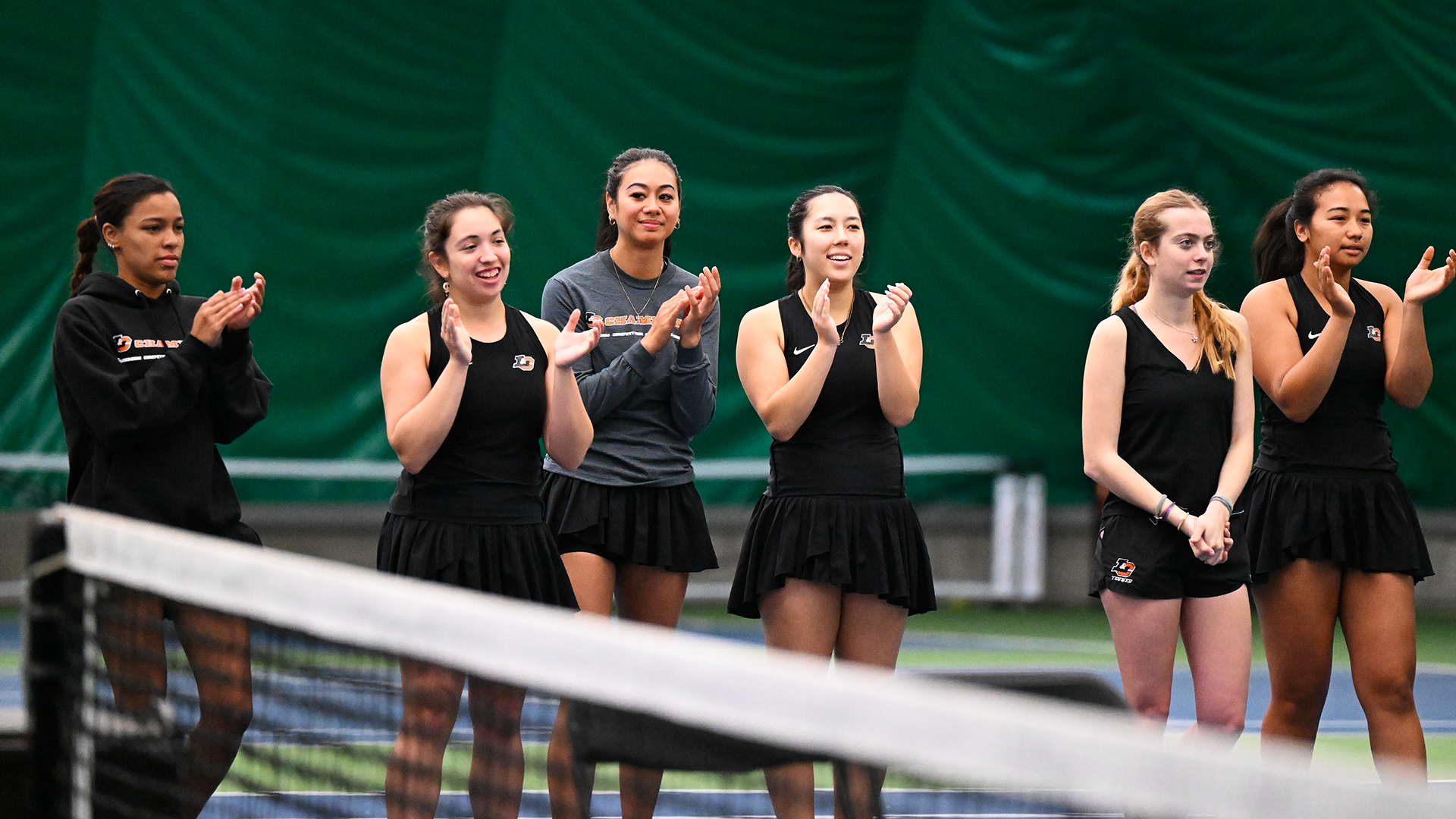 Women's Tennis players cheer on a match from the sideline. 