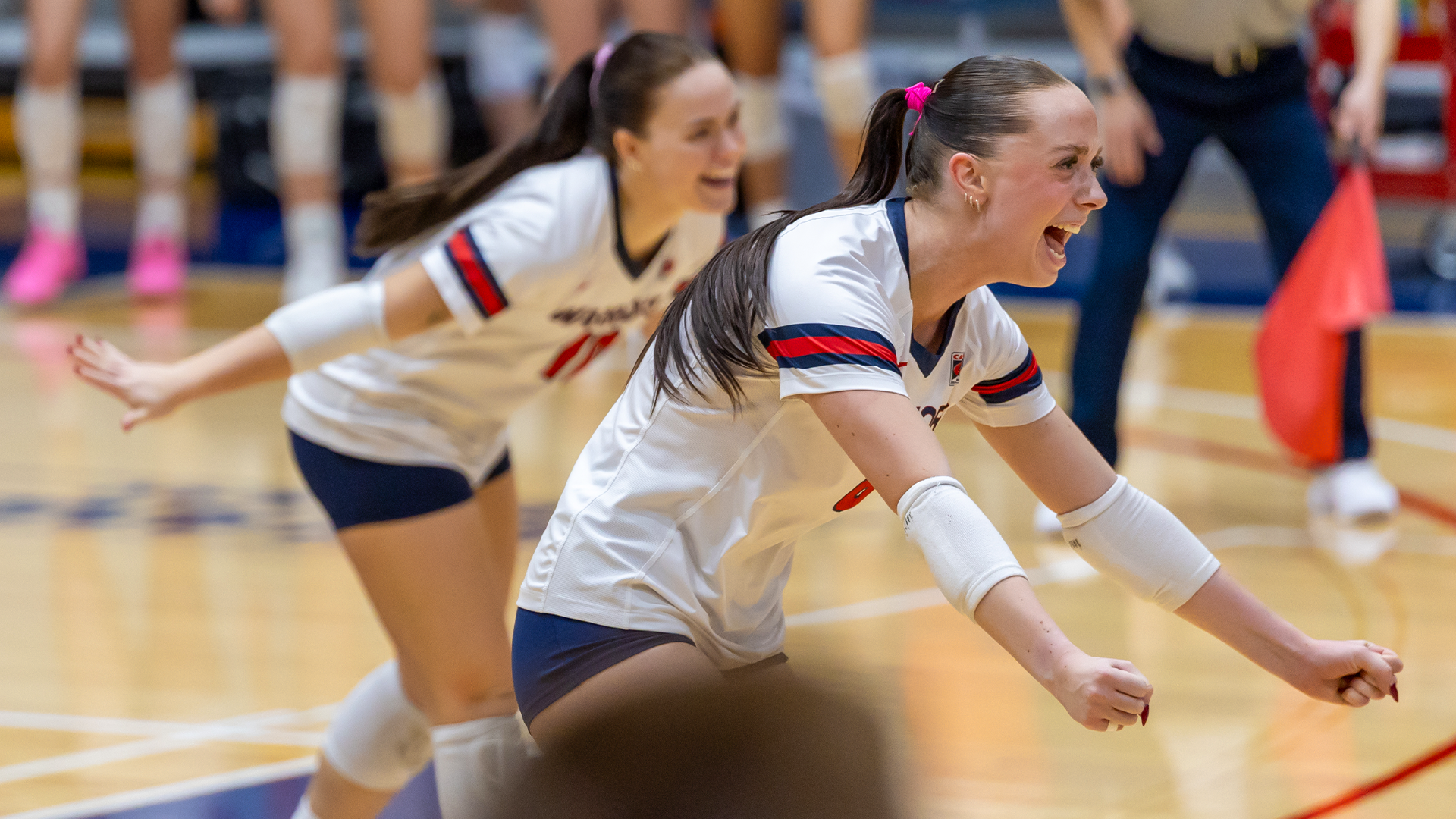 LC State Volleyball players in white jerseys celebrate a point on the court, with one player diving forward in the foreground and teammates visible in the background.