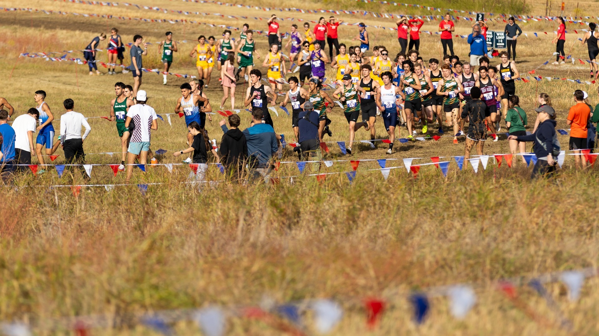 This is a photo of a large group of male athletes running at the 2025 Lone Star Conference Cross Country Championships.