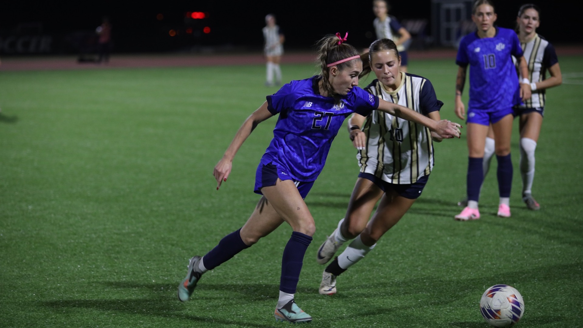 This is a photo of Lubbock Christian forward Claire Jacobson (blue jersey, #27) dribbling the ball past a St. Edward's defender. 