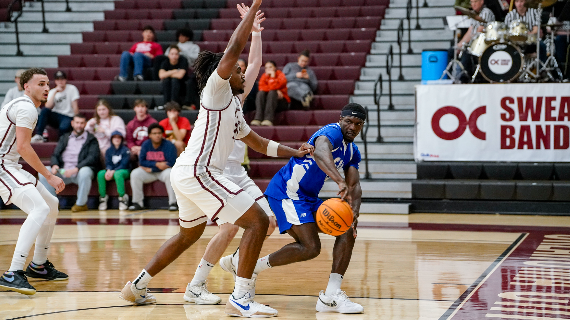This is a photograph of Lubbock Christian forward Alex Anamekwe (blue jersey, #14) passing a basketball around two Oklahoma Christian defenders.