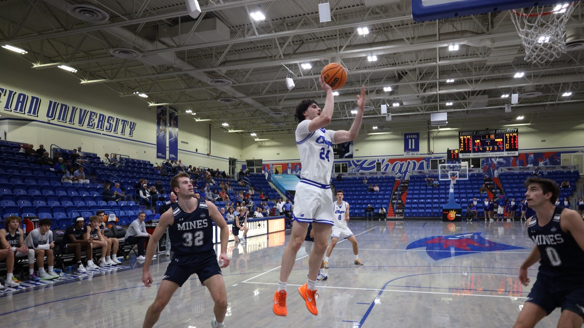 This is a photograph of Lubbock Christian forward Antonio Pusateri (white jersey, #24) shooting a basketball over a Colorado School of Mines defender. 