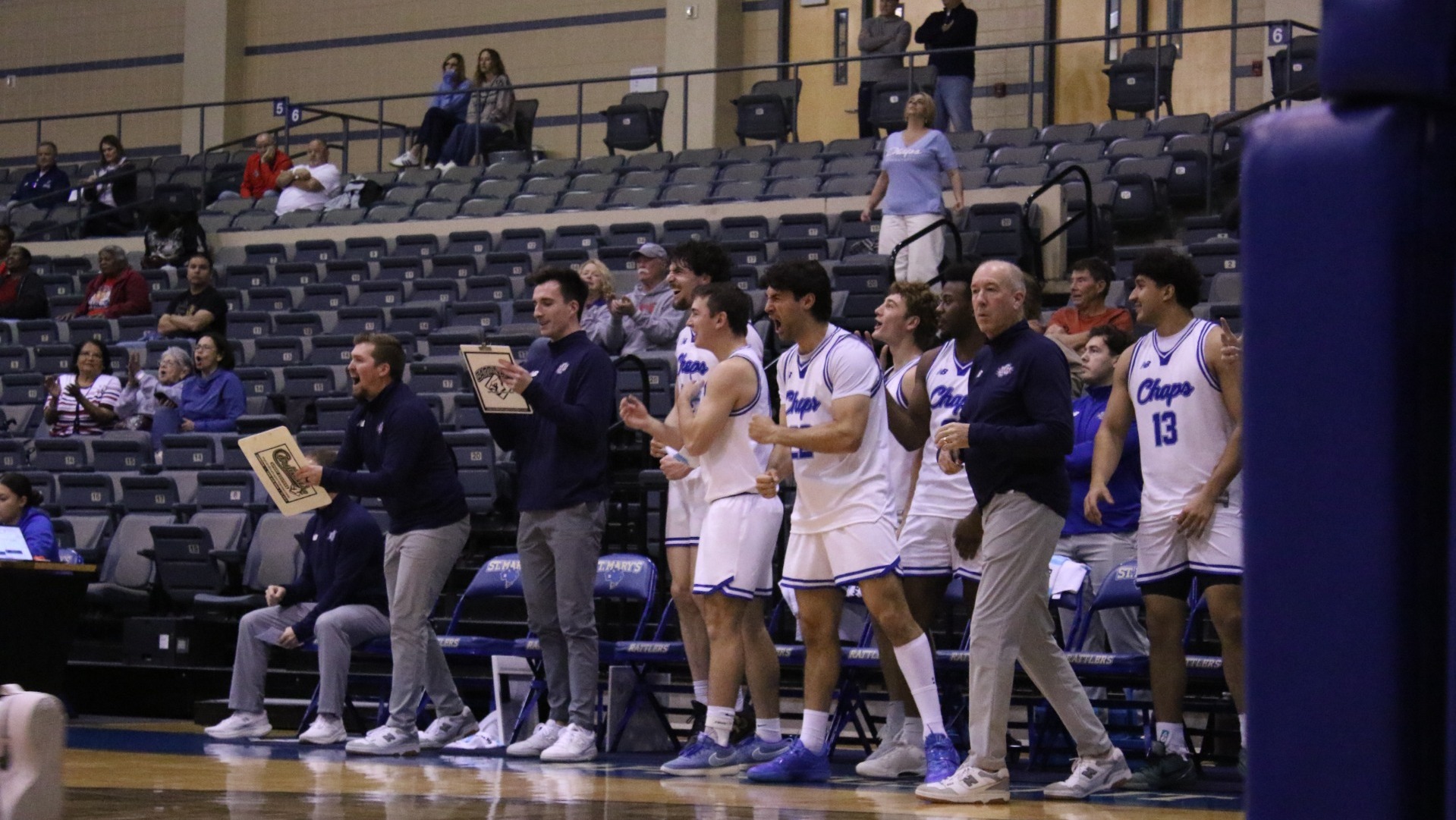 This is a photograph of members of the Lubbock Christian men's basketball team on the bench celebrating after a made basket by one of their teammates. 