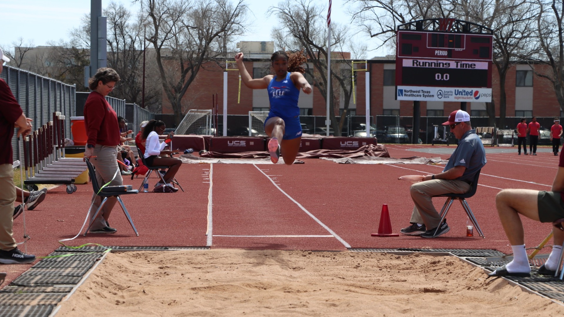 Photo of Lubbock Christian University track athlete, Faizah Ford, jumping during the West Texas Relays. Ford is seen mid-jump, leaping toward the camera above a sand pit. She is wearing a blue LCU track uniform.