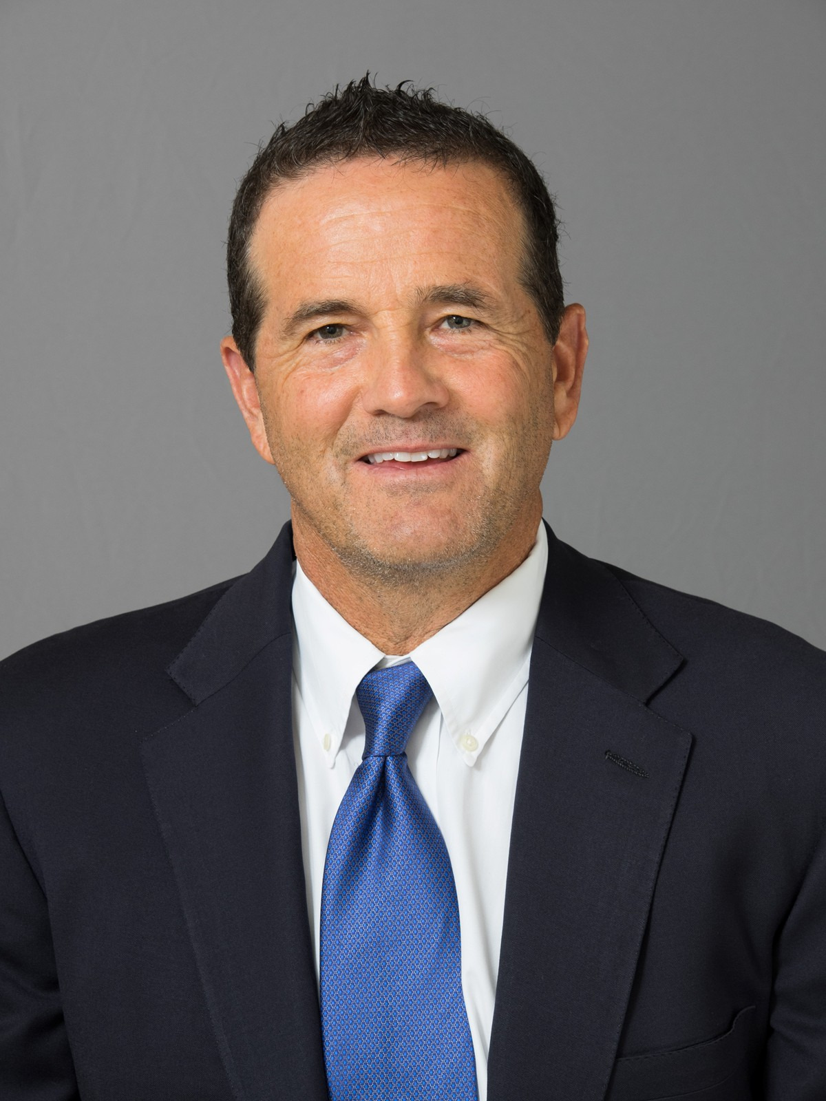 Head shot image of Hutton Jones wearing a dark suit and bright blue tie with shade of purple glare