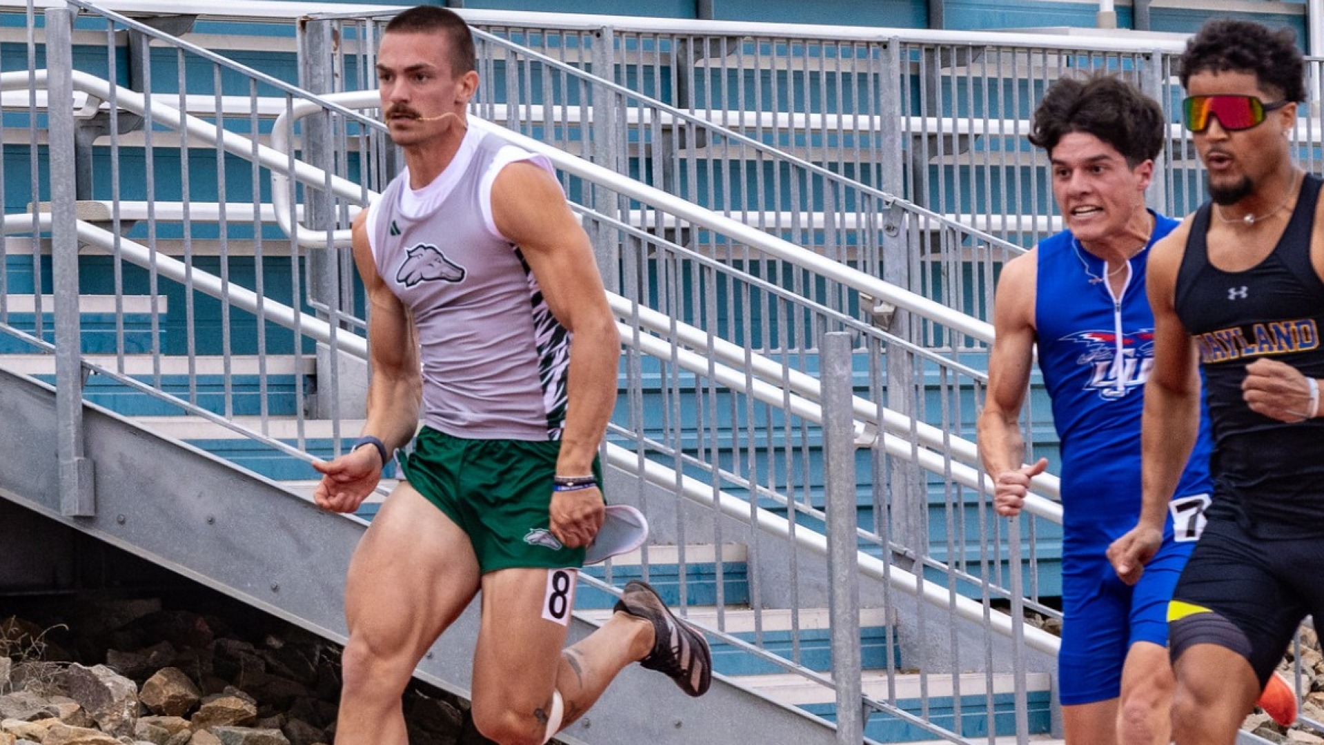 Photo of Lubbock Christian University track athlete, Kole Carrasco, running during the Greyhound Open. Carrasco is seen with two other runners, as they are running down the track. He is wearing a blue LCU tracksuit.
