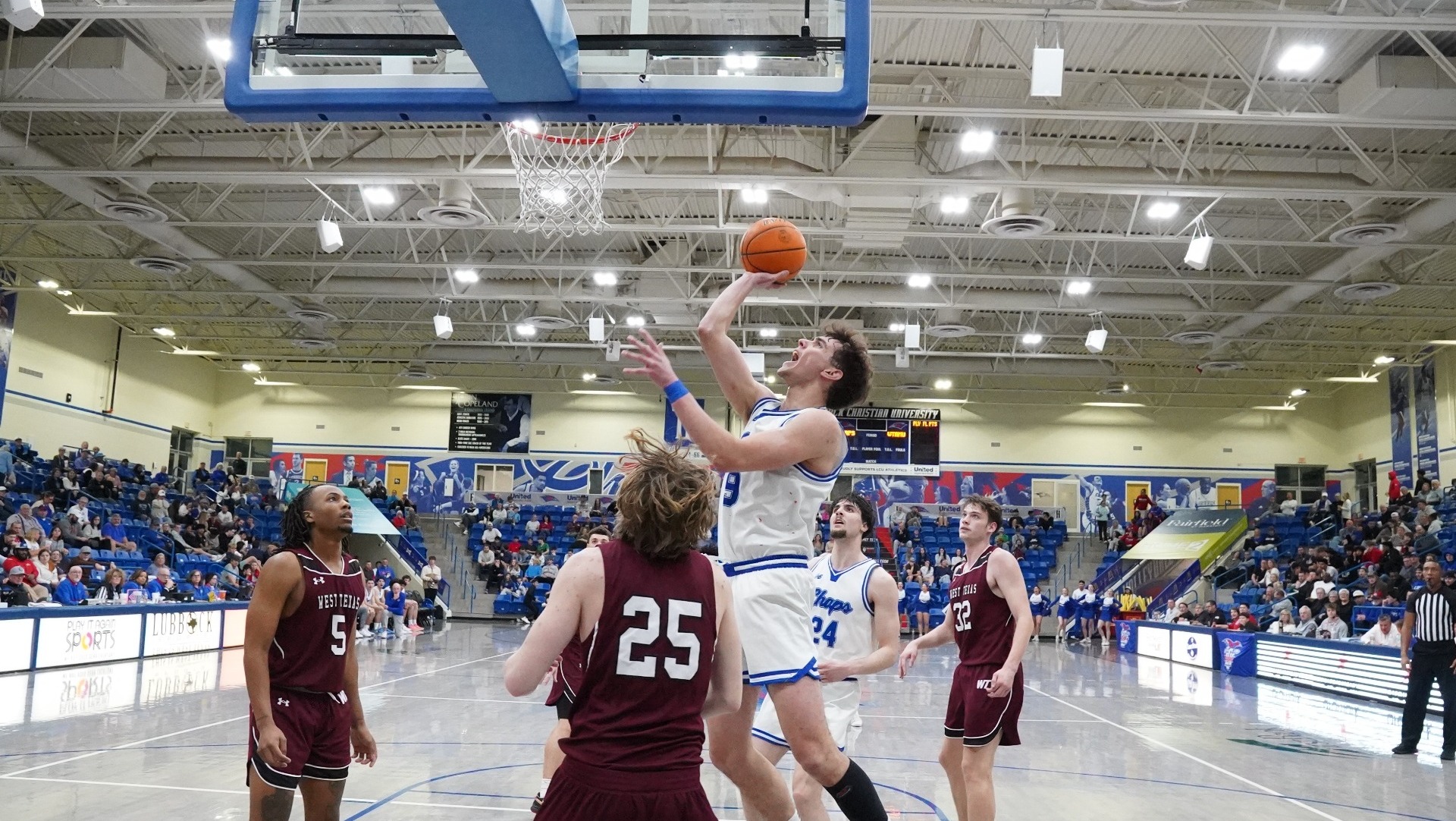 This is a photograph of LCU guard Lucas Mercandino (white jersey, #9) shooting a layup over a West Texas A&M defender (maroon jersey) during a game at the Rip Griffin Center. 