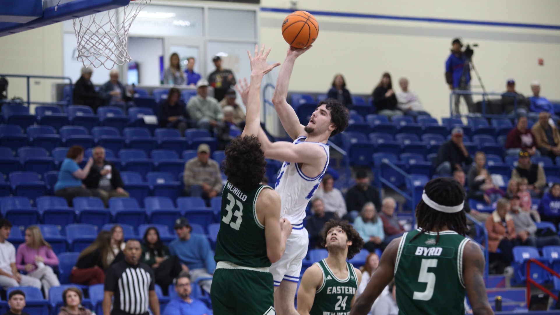 This is a photo of Lubbock Christian forward Antonio Pusateri (white jersey, #24) shooting over an Eastern New Mexico defender (green jersey) at the Rip Griffin Center. 