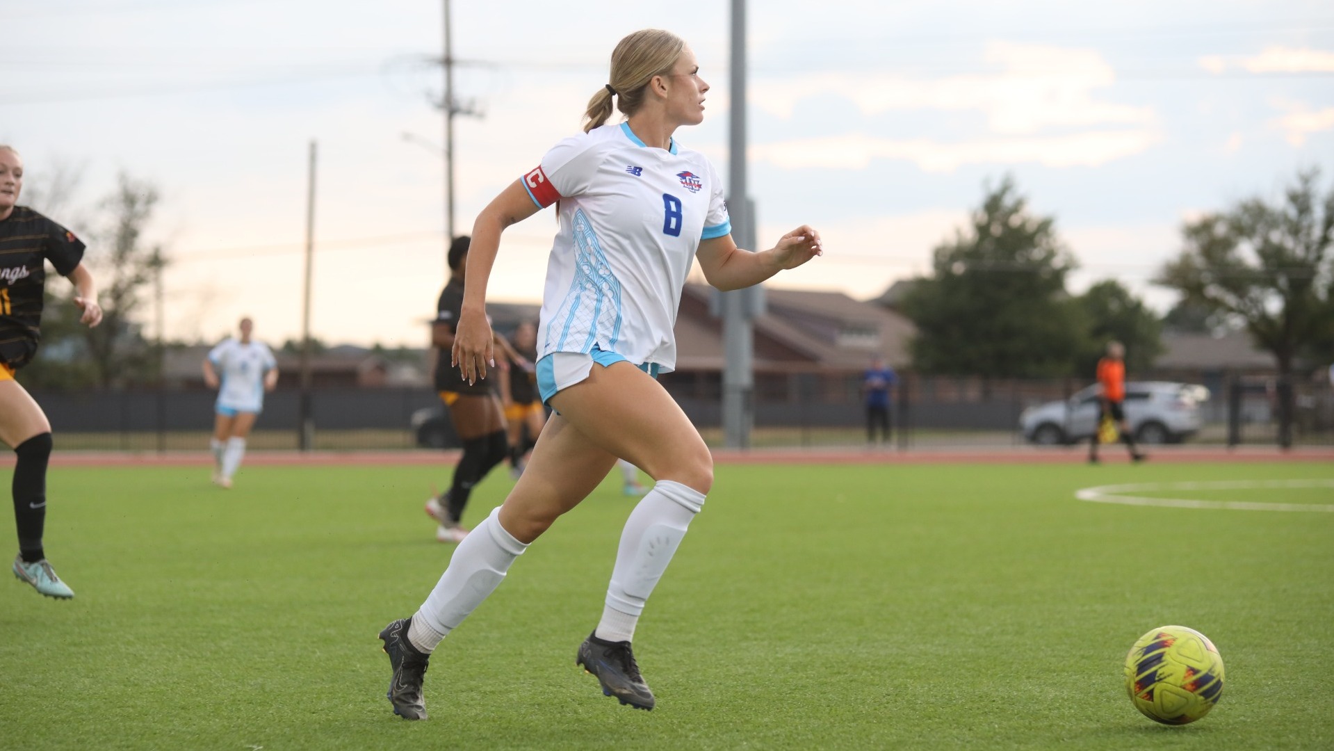 This is a photo of Lubbock Christian women's soccer player Casey Storer (white jersey, #8) dribbling a yellow soccer ball up the field.