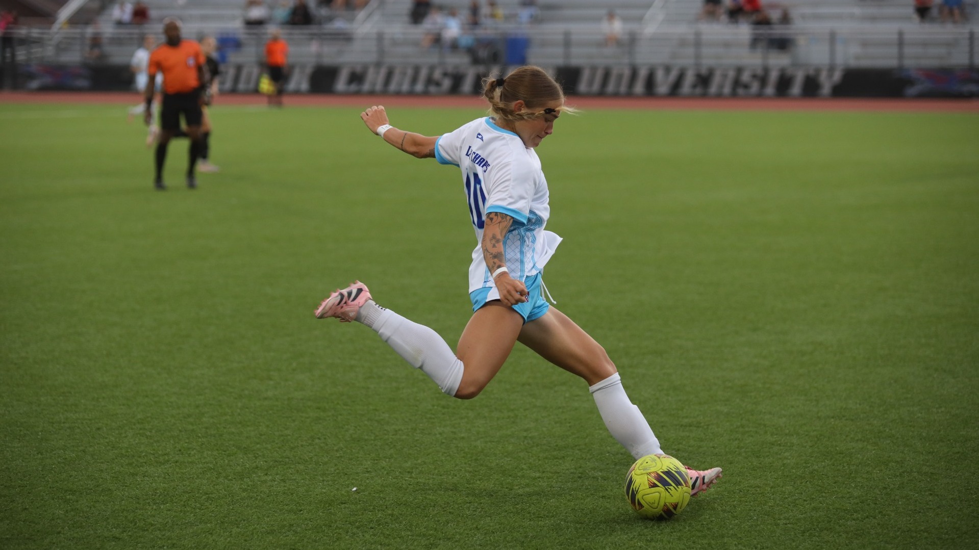 This is a photo of Lubbock Christian midfielder Journey Curs (white jersey, #10) preparing to kick a yellow soccer ball.