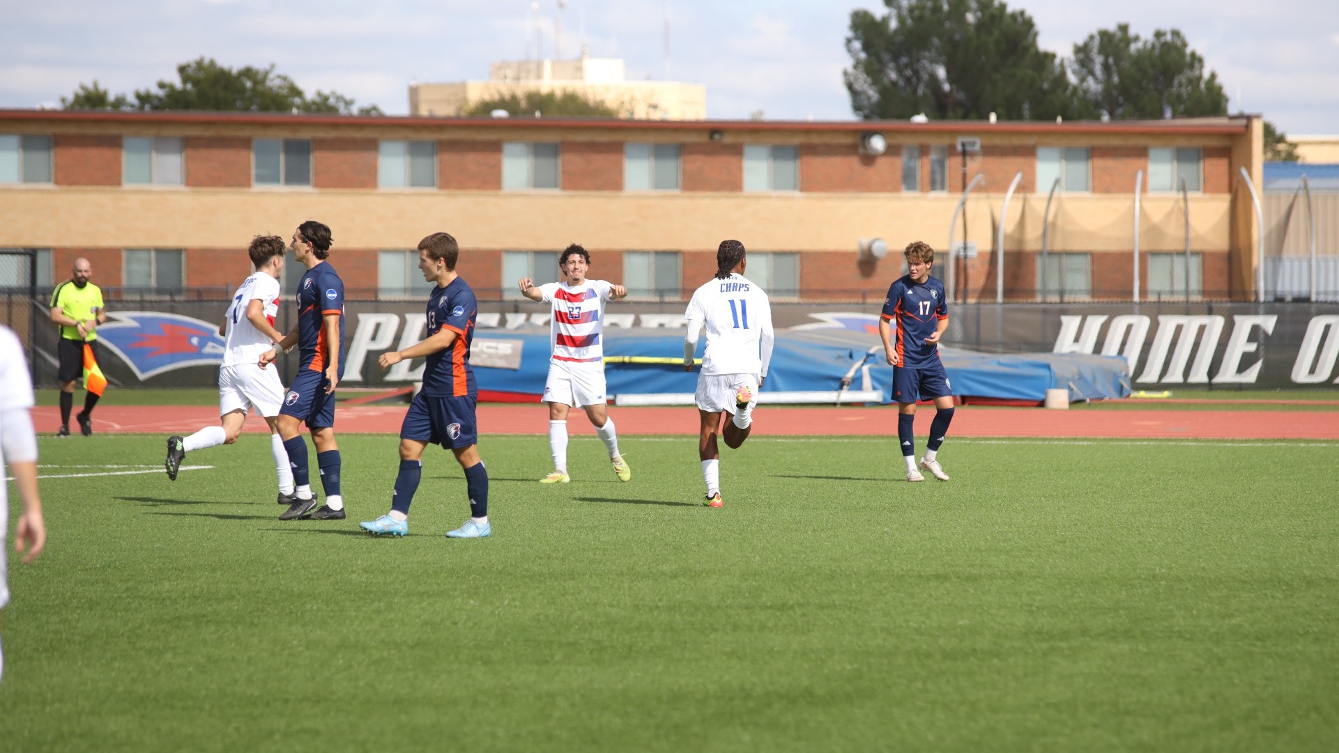 This is a photo of Lubbock Christian midfielder Junior Lopez (white jersey, #23) celebrating with forward Augusto Militao (white jersey, #11) after a goal at the LCU Soccer & Track Complex. 