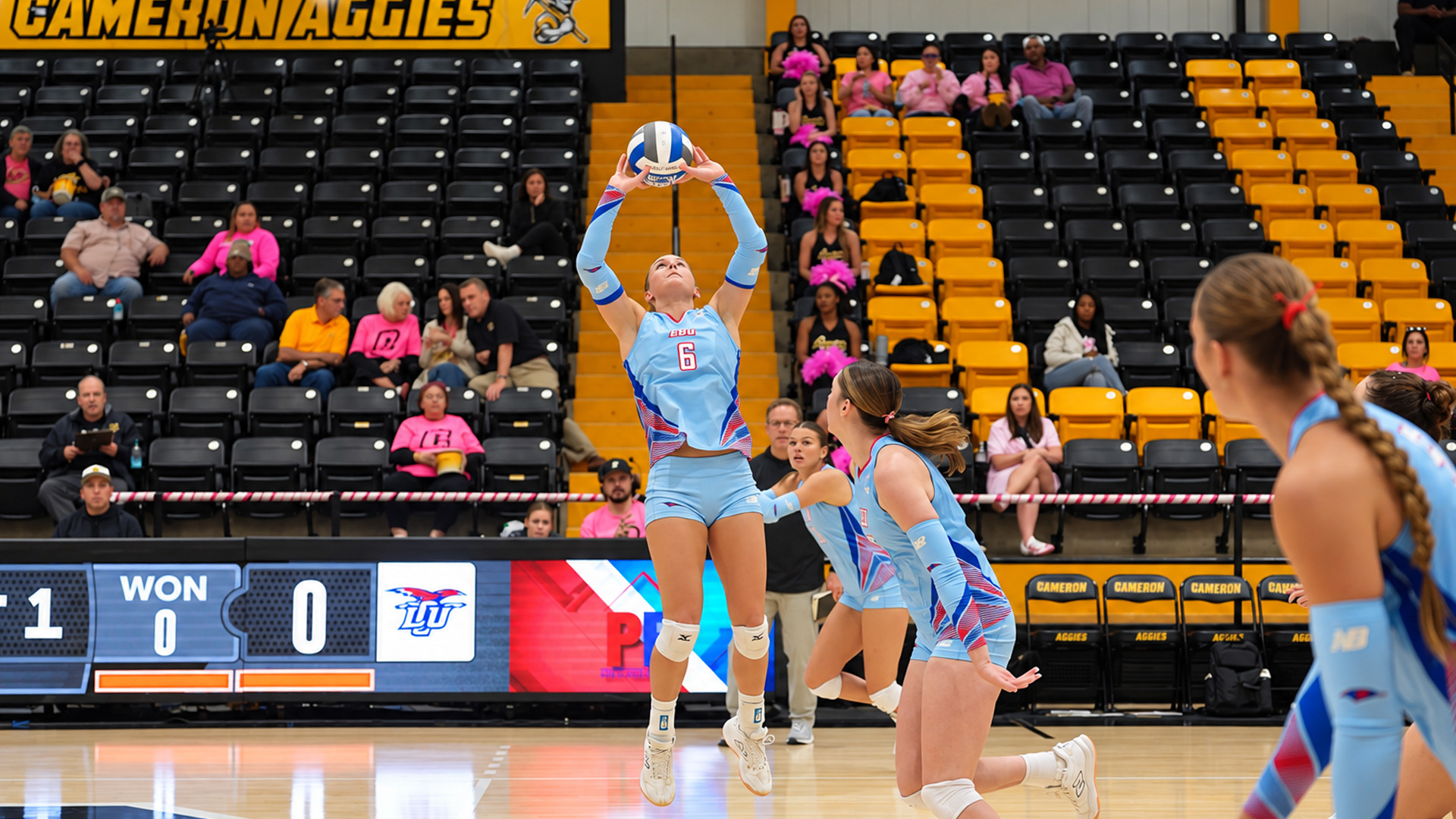 Action photo of LCU player #6, in a light blue jersey, jumping to set the ball with both hands overhead, with teammates moving into position nearby. The scoreboard reads 