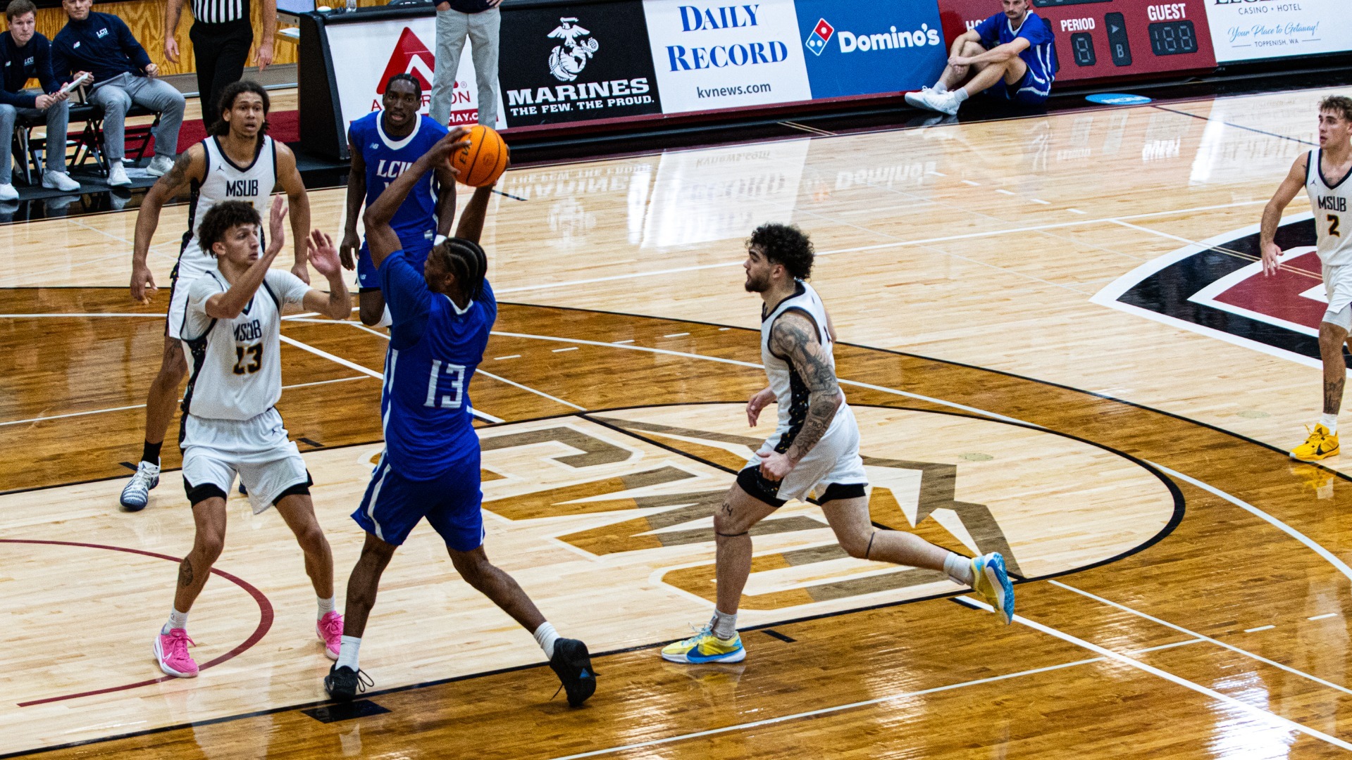 This is a photo of Lubbock Christian guard DeAndre Lott (blue jersey, #13) jumping up to shoot a layup during a game against MSU-Billings.