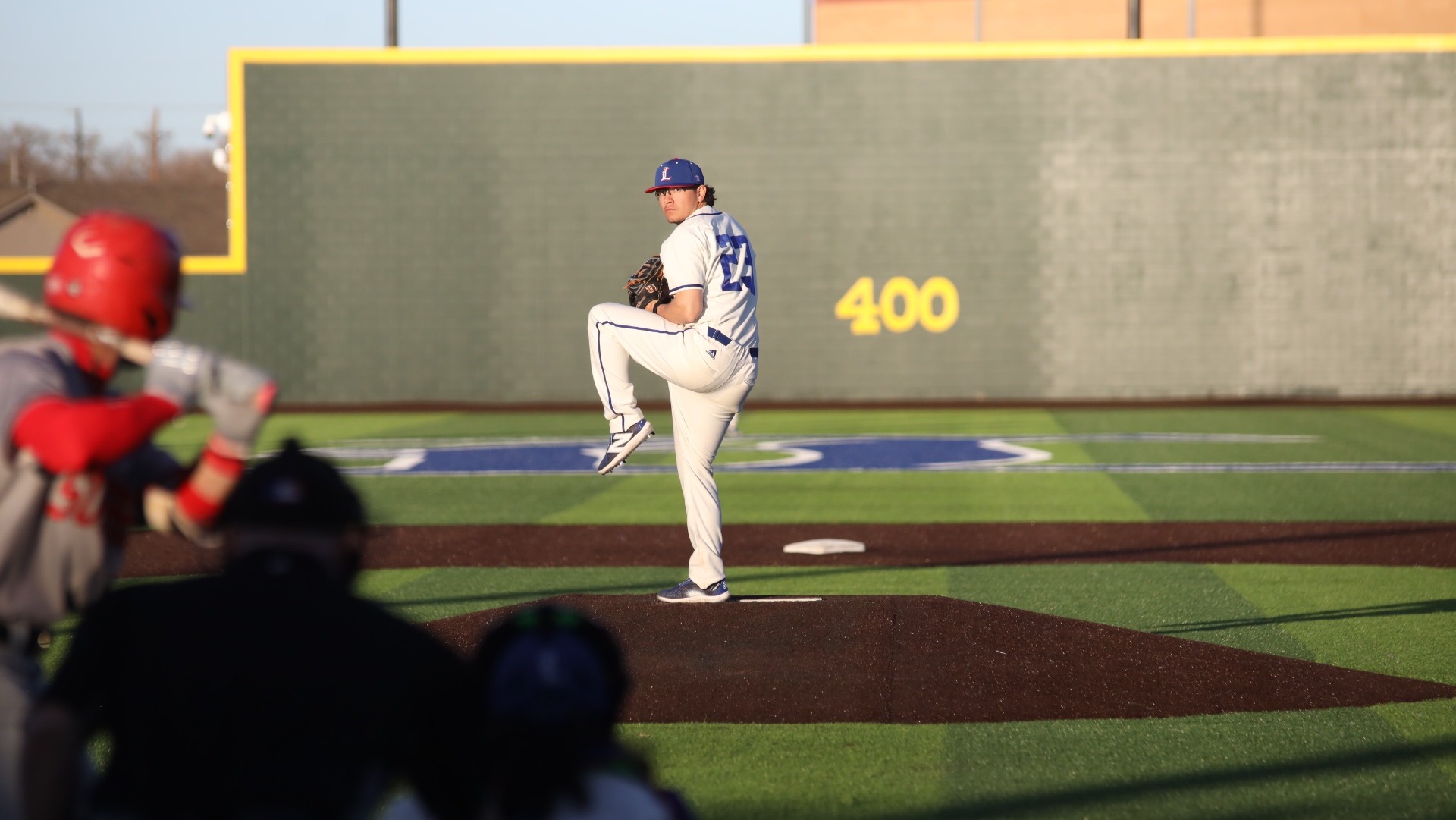 This is a photo of Lubbock Christian pitcher Aaron Rubio (white jersey, #23) winding up to throw a pitch during a game at Hays Field.