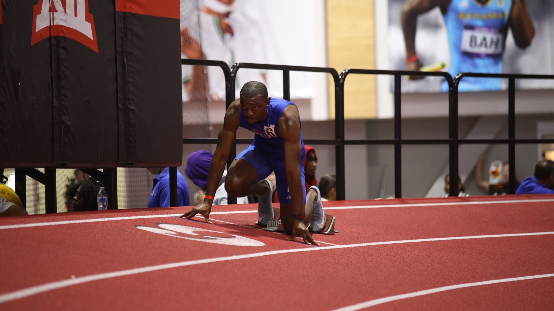 This is a photo of Lubbock Christian athlete Reuel Campbell (blue uniform) kneeling in the starting blocks on a track prior to a race. 