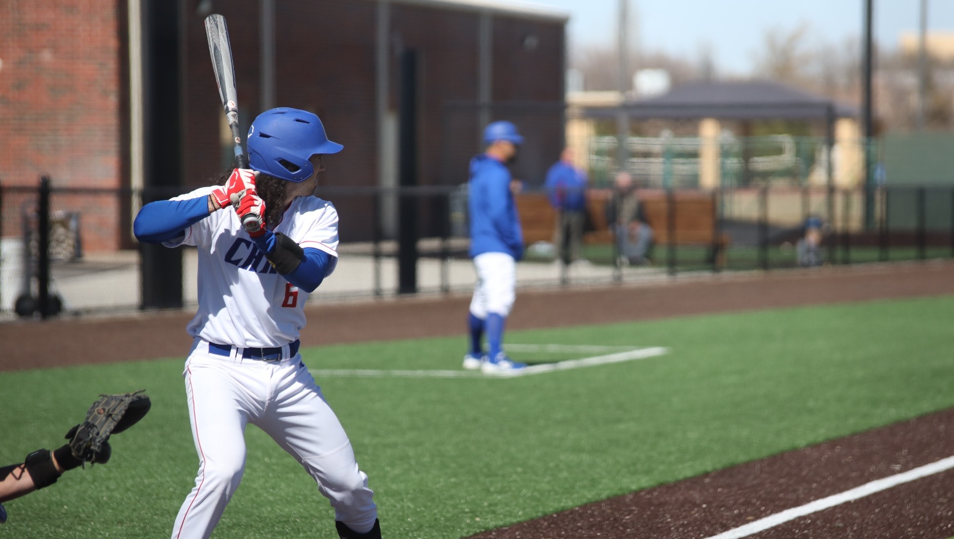 This is a photo of Lubbock Christian catcher Jorge De Los Santos (white uniform, #6) preparing to swing at a pitch during a game at Hays Field.