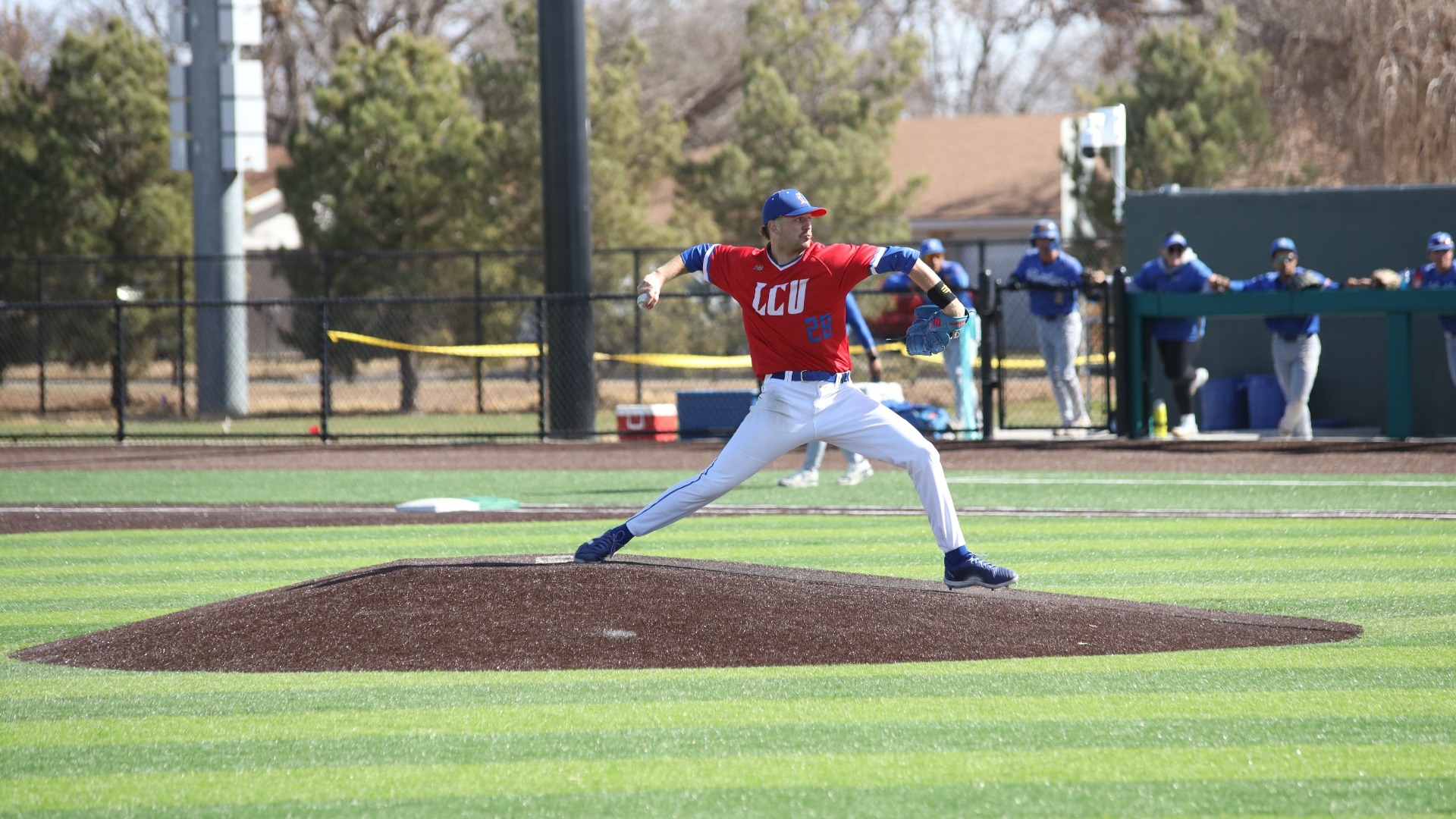 This is a photograph of Lubbock Christian pitcher Caden Cline (red jersey, #28) throwing a pitch off the mound at Hays Field.