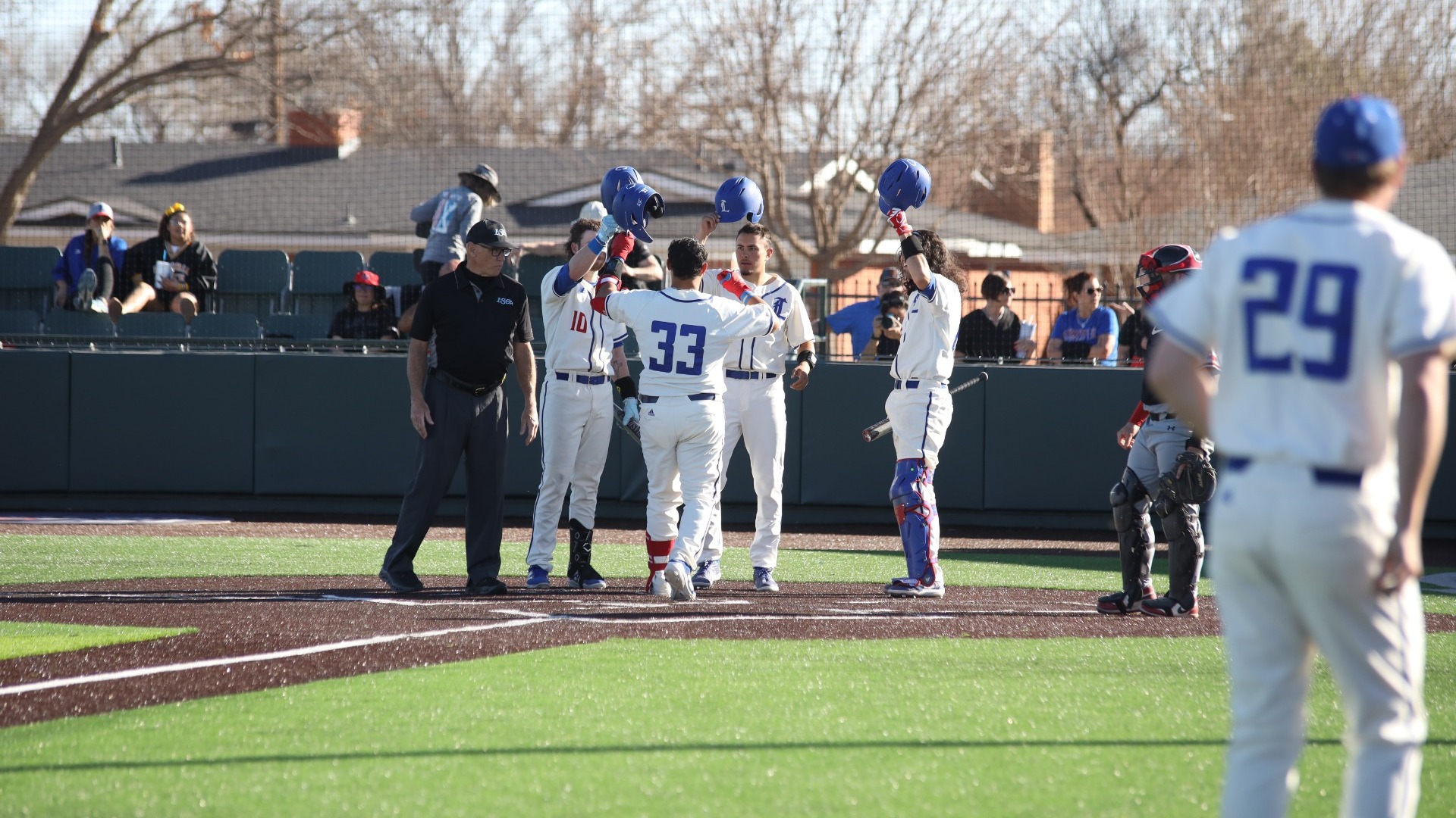 This is a photo of Johnny Gomez III (white jersey, #33), celebrating with teammates after hitting a home run at Hays Field. 