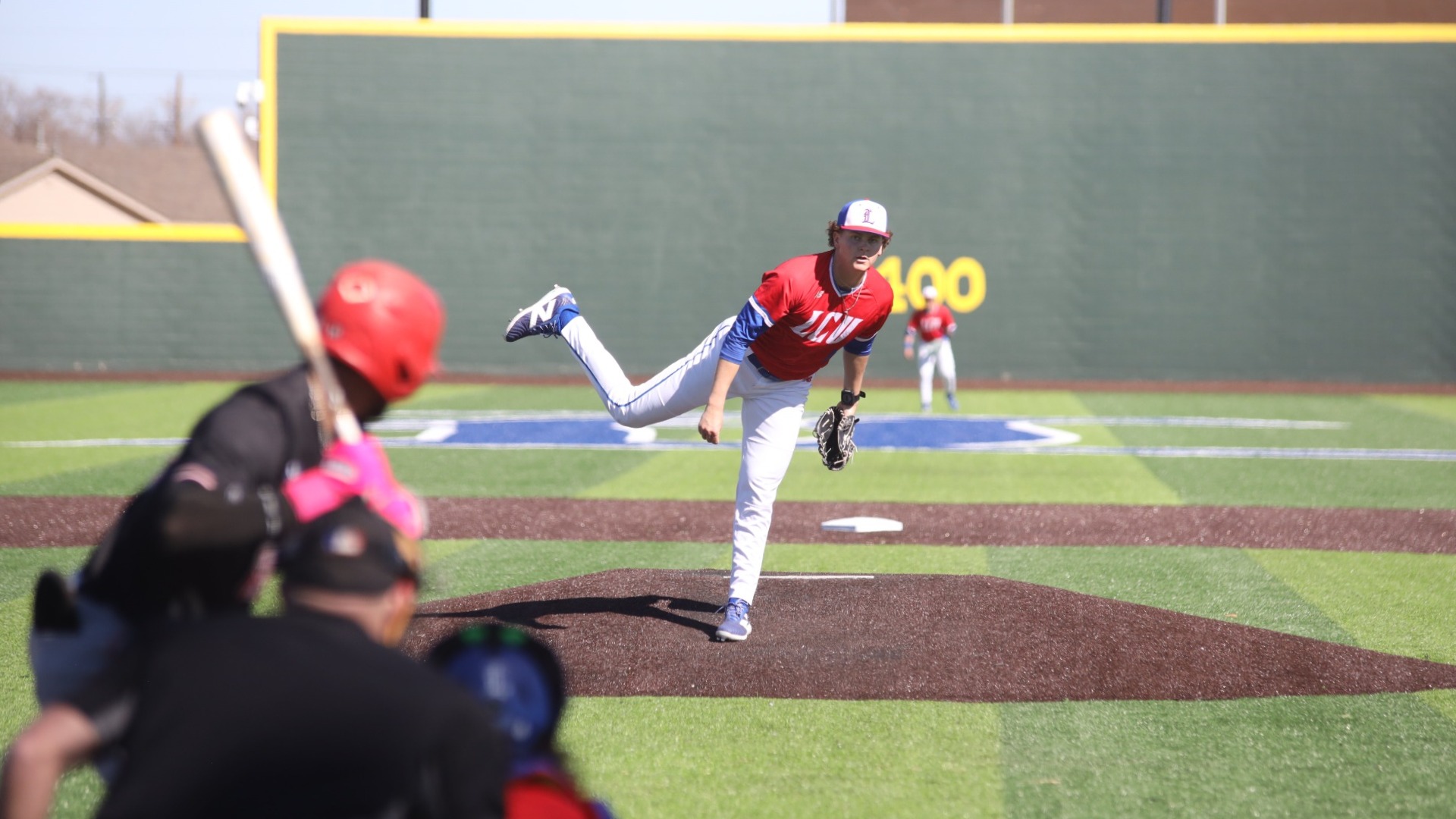 This is a photo of LCU pitcher Karson Dunn (red jersey #19), right after he has released a pitch during a game at Hays Field. 