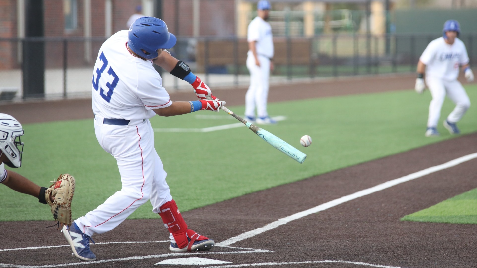 This is a photograph of Lubbock Christian batter Johnny Gomez III (white jersey, #33) hitting the ball during a game at Hays Field. 