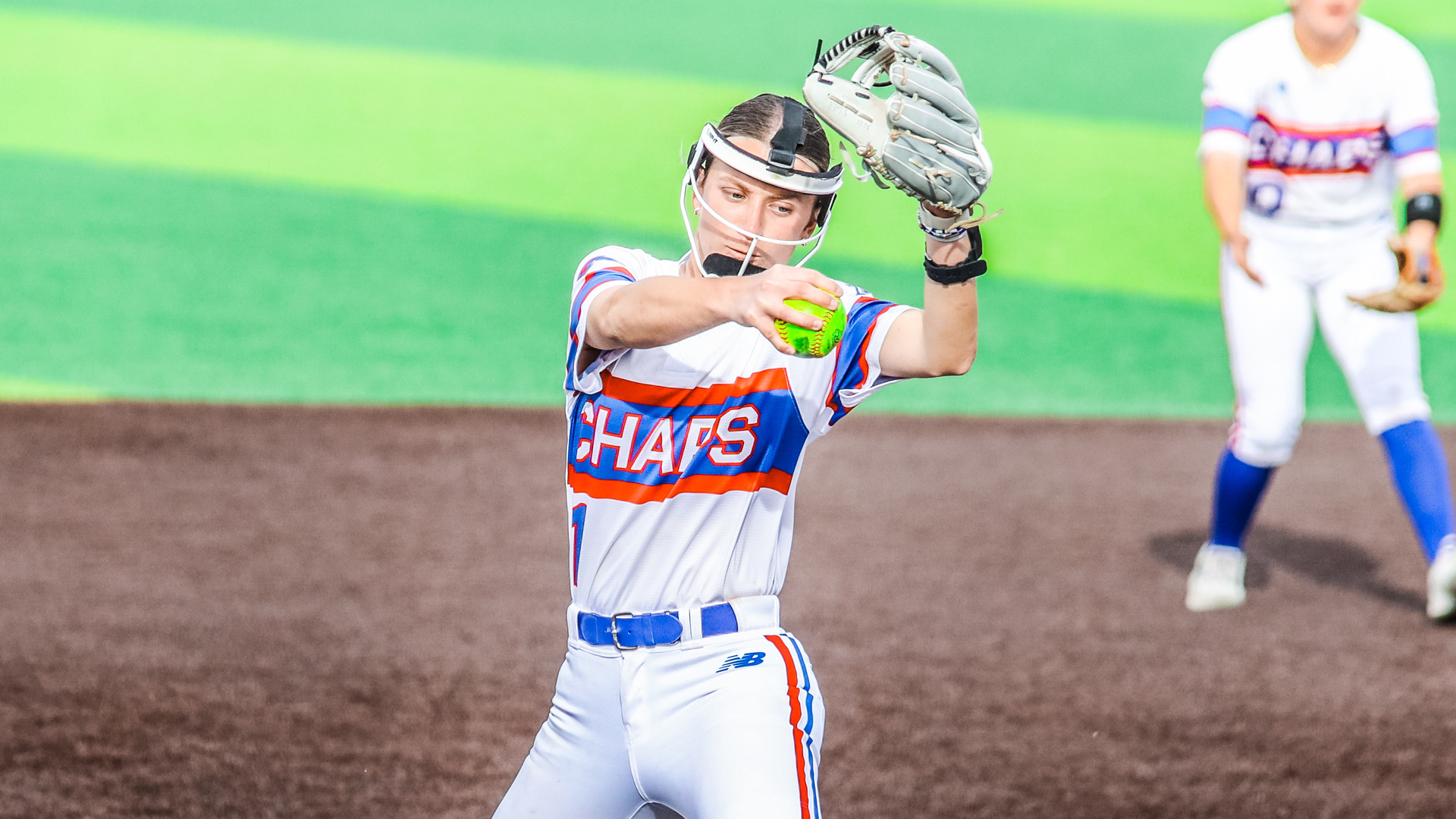 An LCU Lady Chaps infielder in a white Chaps uniform fields a ball and prepares to make a throw at Maner Park, with a teammate visible in the background