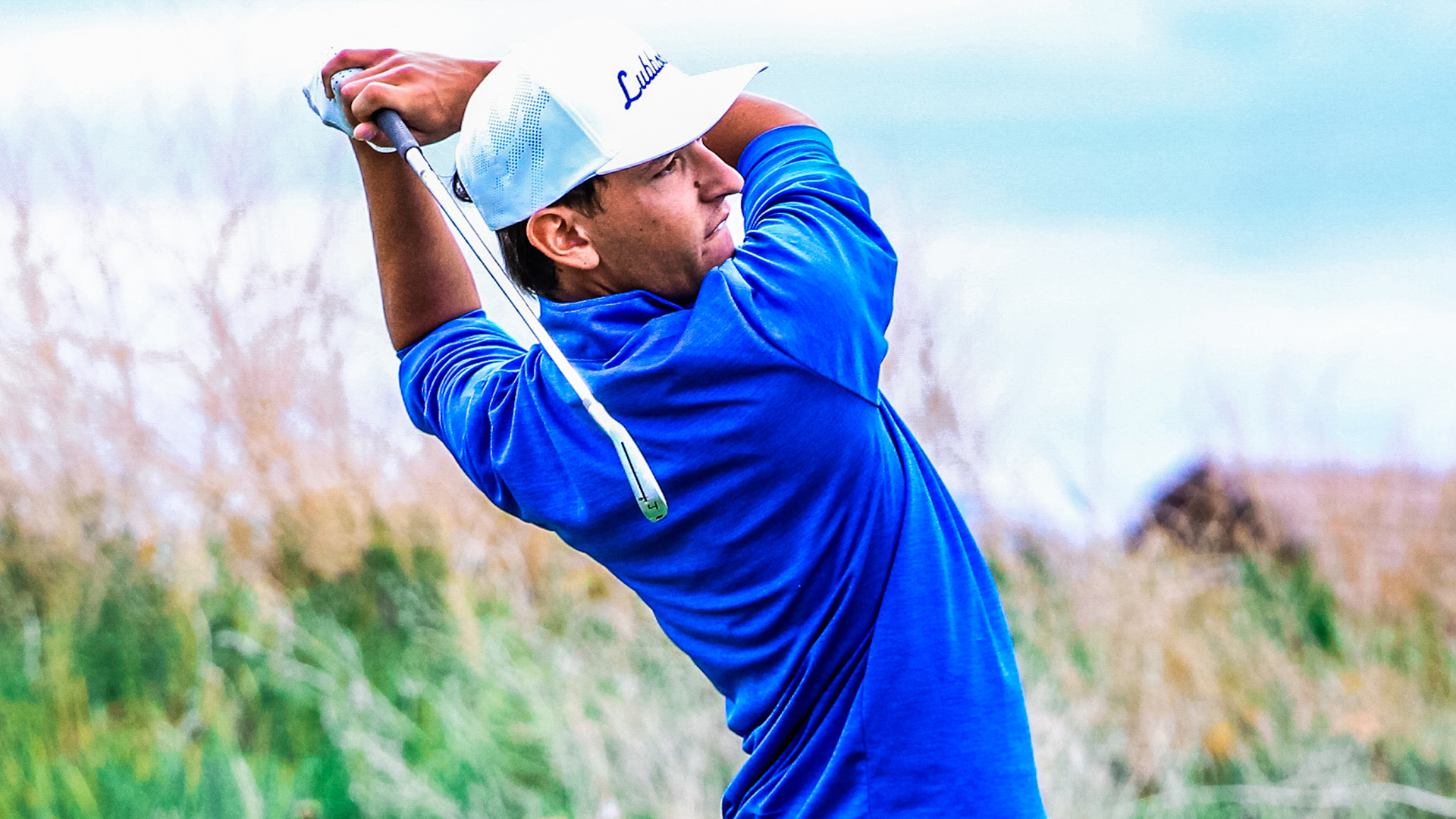 Close uo image of a golfer in his follow-through wearing a royal blue shirt with white golf hat.