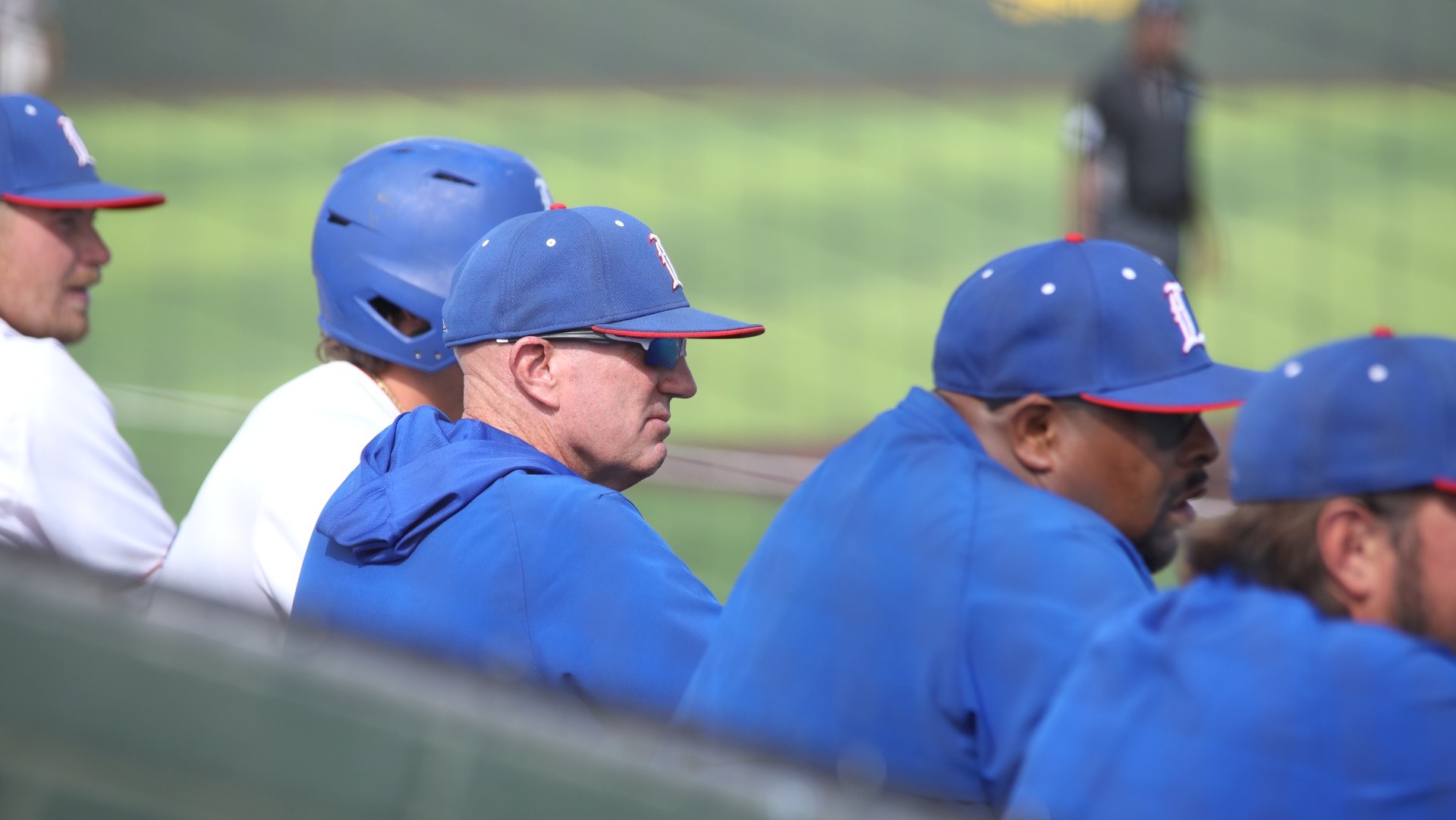 This is a photo of the Lubbock Christian baseball coaching staff, wearing blue shirts and blue hats, watching game action from the dugout at Hays Field. 